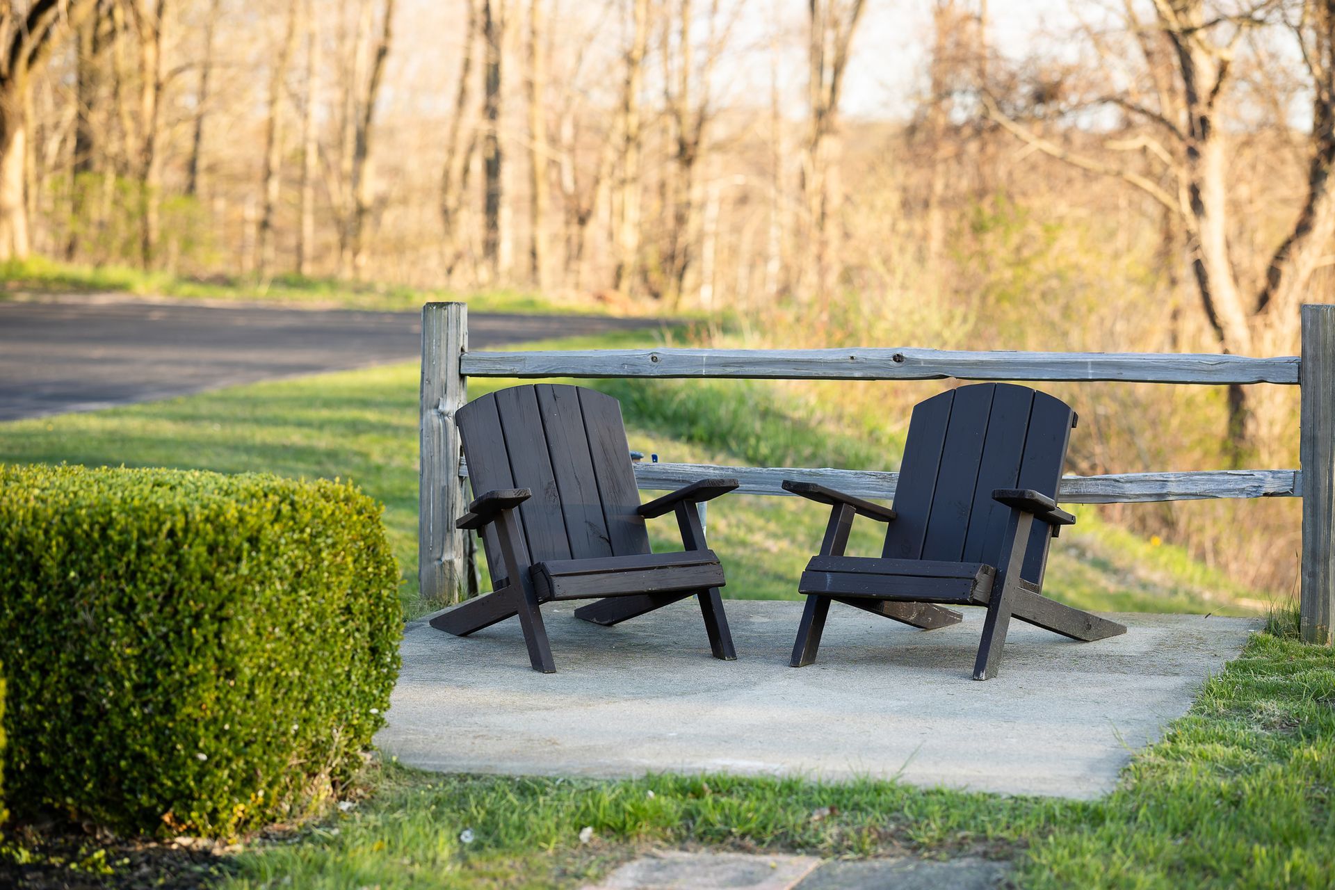 Two black adirondack chairs are sitting on a concrete patio next to a wooden fence.