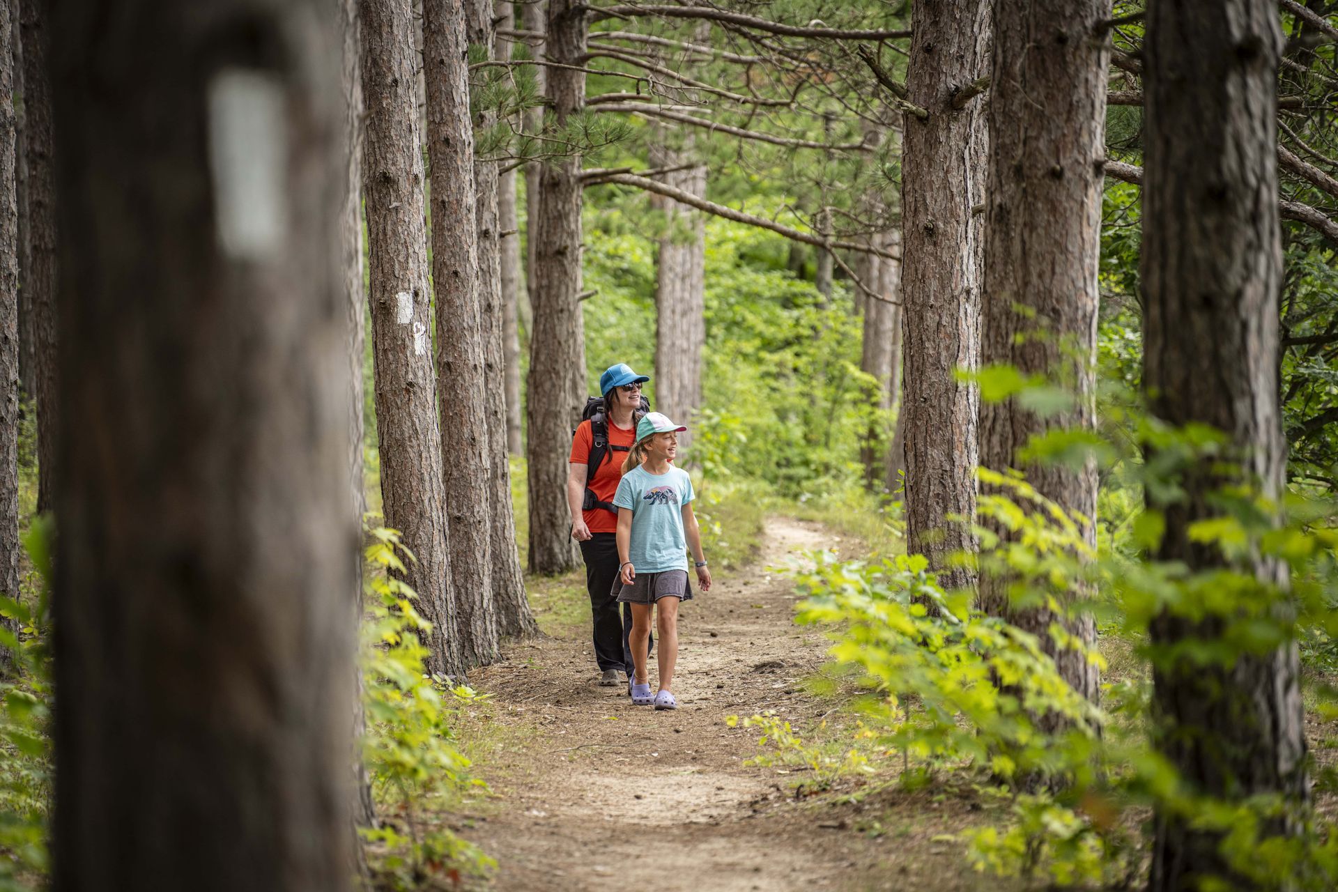 A woman and a child are walking down a trail in the woods.