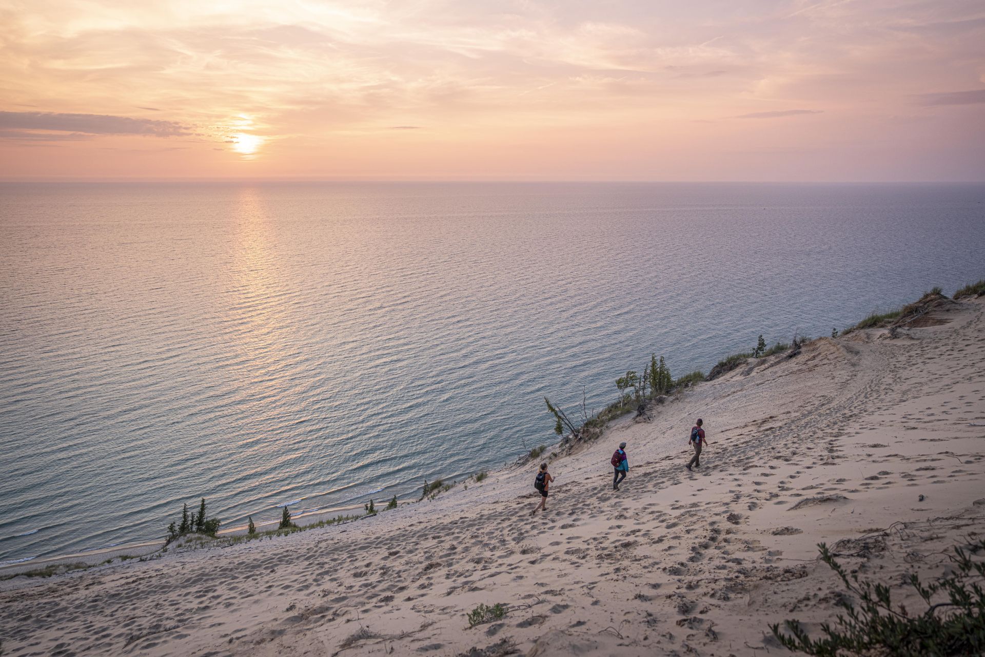 A group of people are walking up a sand dune overlooking the ocean at sunset.