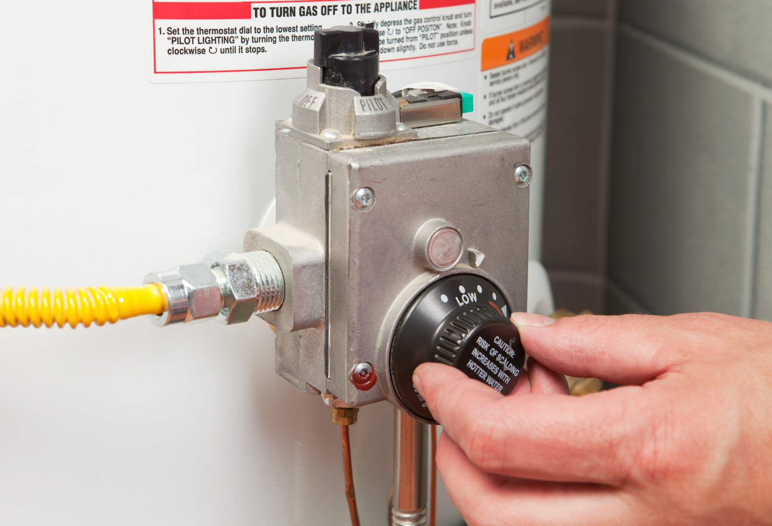 A person is adjusting a thermostat on a water heater.