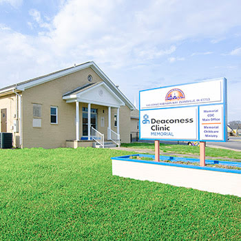 A tan, one-story Deaconess Clinic building with a white sign in front, located under a blue sky with light clouds.