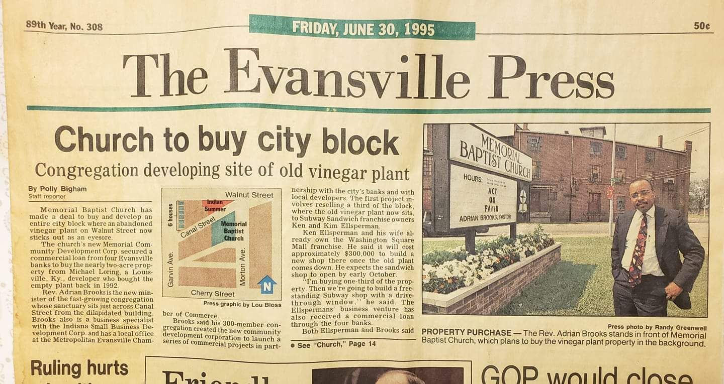 A red brick building with a gabled roof, a front portico with white columns, and a concrete walkway leading to the doors.