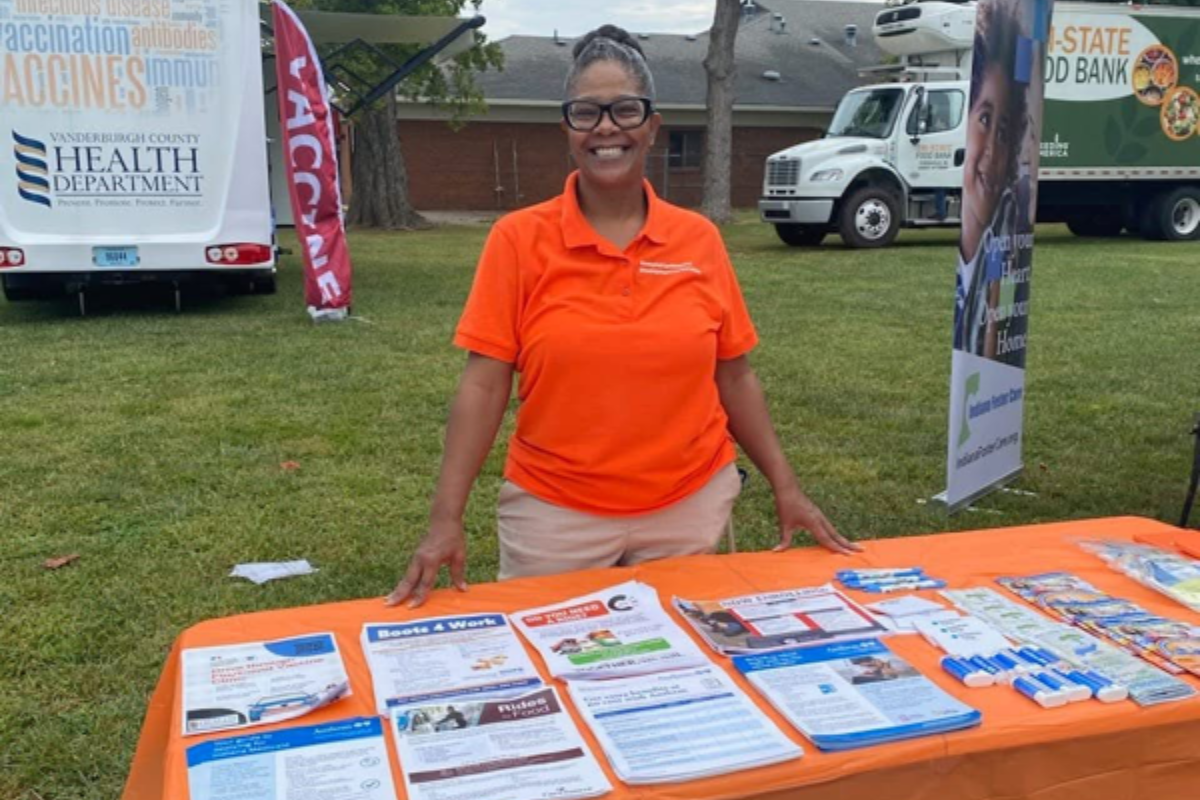 Four people sitting at a wooden conference table in an office, laughing while working on laptops and tablets.