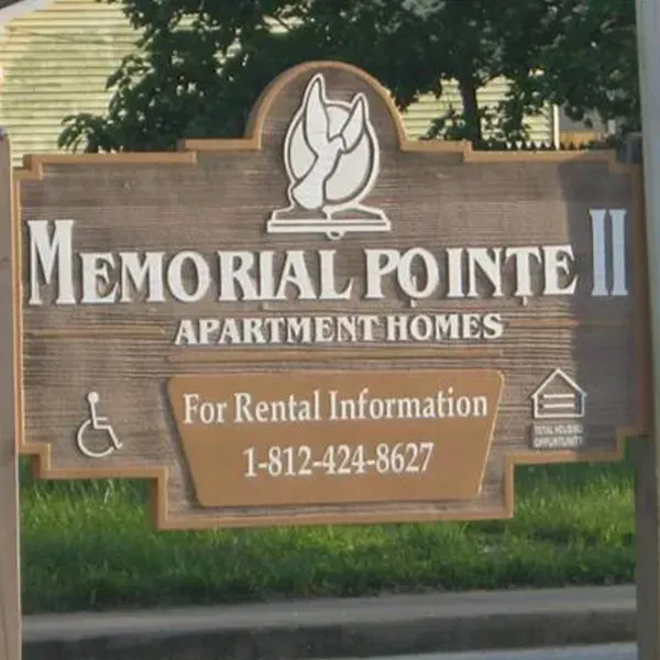 A wood-toned sign for Memorial Pointe II Apartment Homes with a phone number and an accessibility icon.
