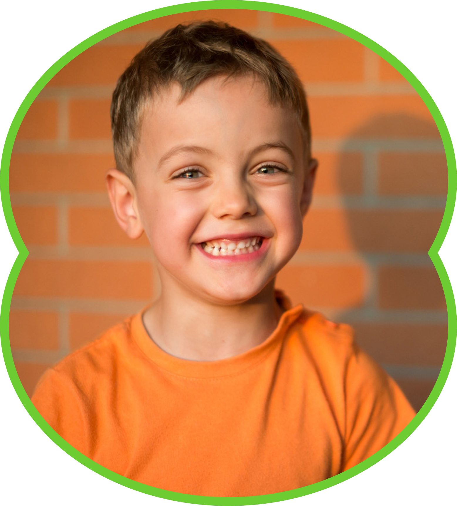 Smiling child in orange shirt in front of a brick wall, framed by a green circle.