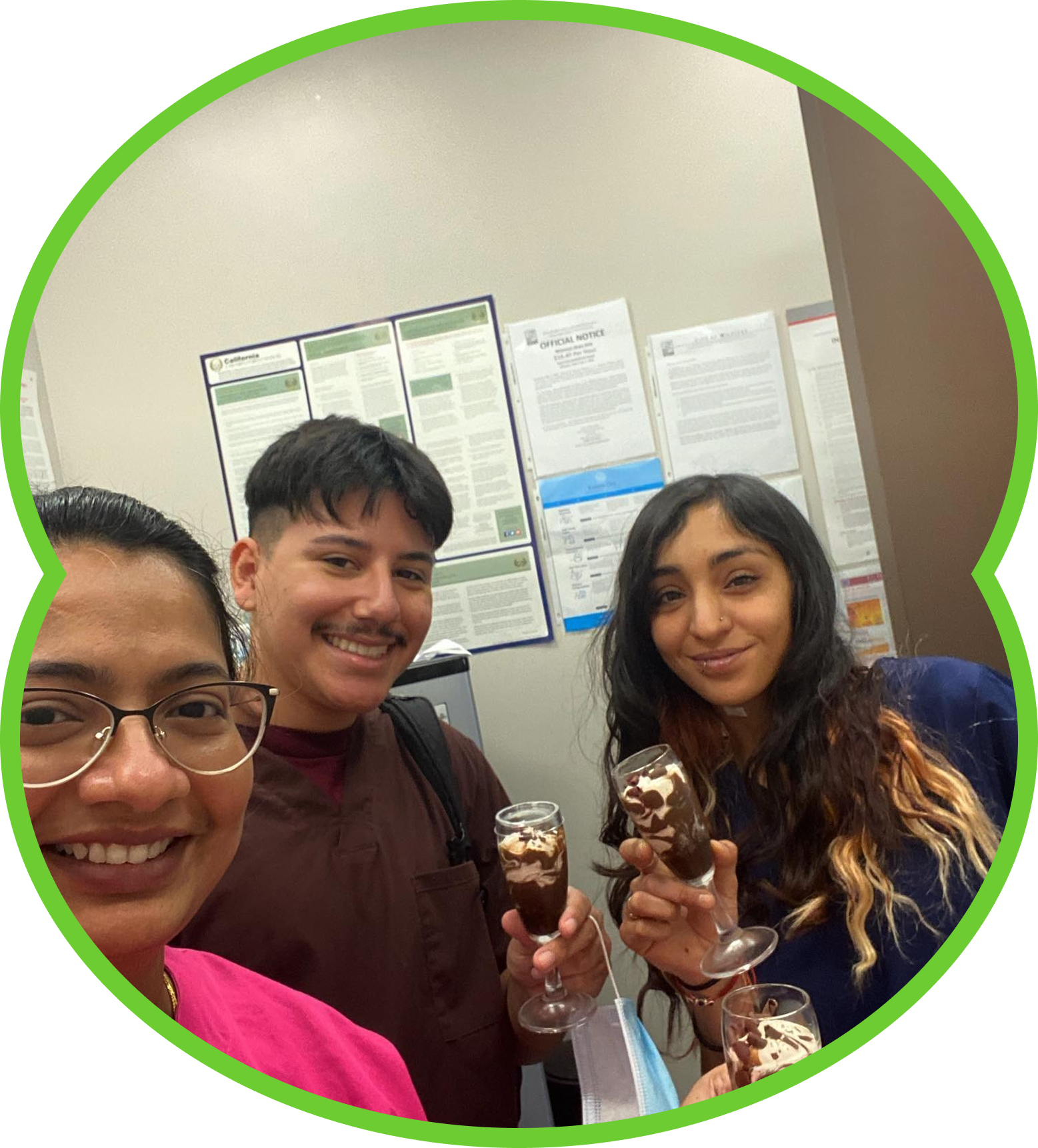 Three people smiling and holding chocolate desserts in a room with posters on the wall.