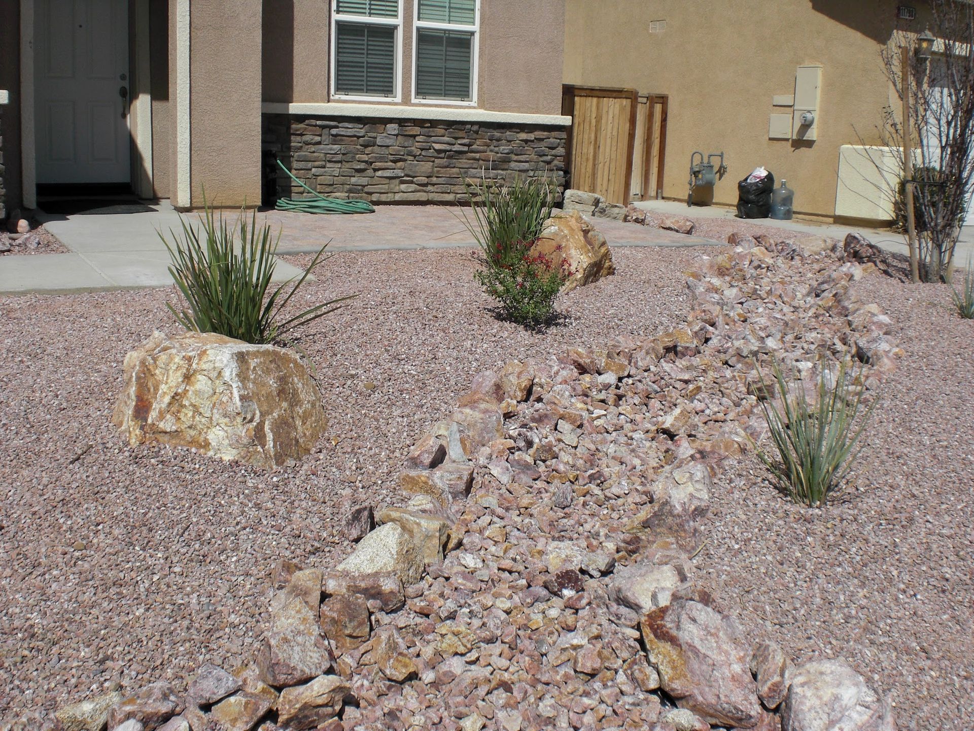 Front yard with gravel, rocks, and small desert plants; beige house with stone accent.