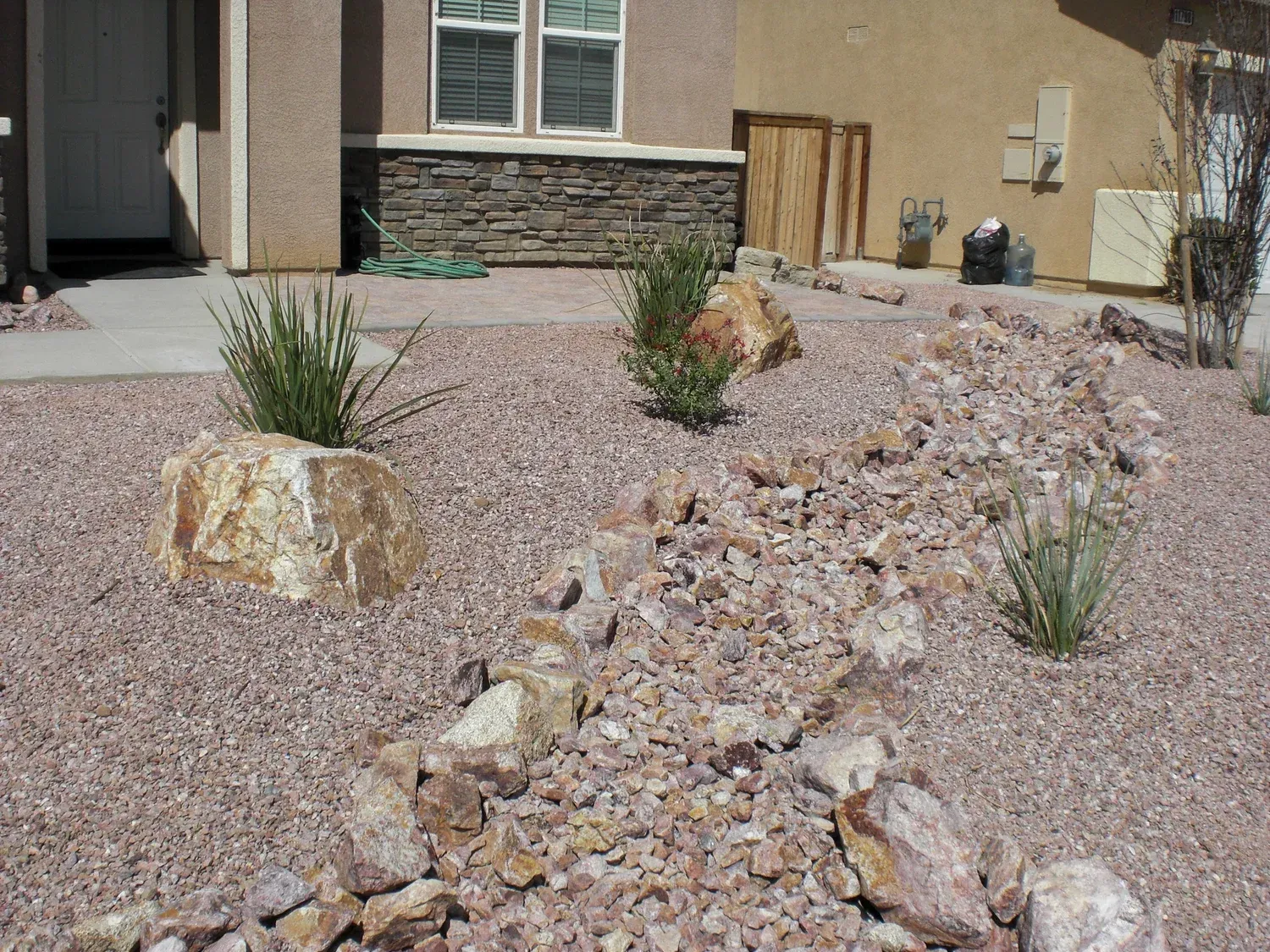 Desert landscape with gravel, large rocks, and sparse green plants.