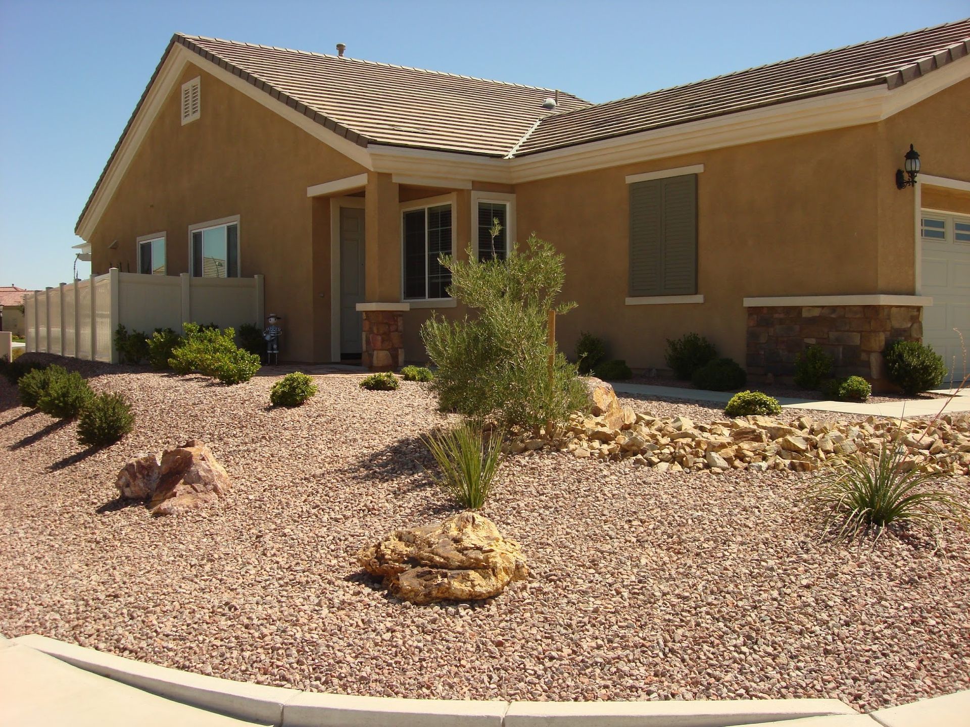 Tan house with xeriscaped front yard, including gravel, rocks, and small plants.