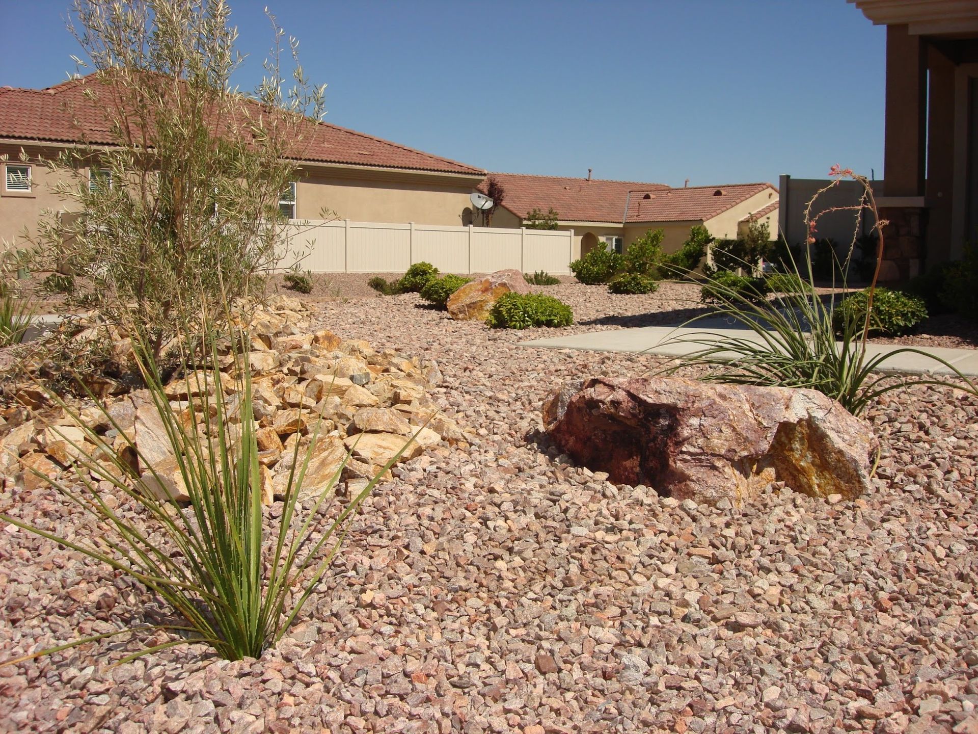Desert landscaping with rock ground cover, boulders, and sparse plants.