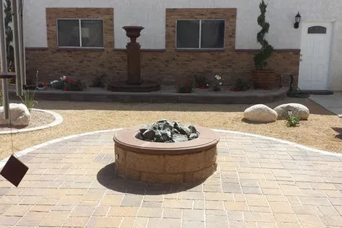 Brick patio with a fire pit, fountain, and potted plants in a courtyard setting.