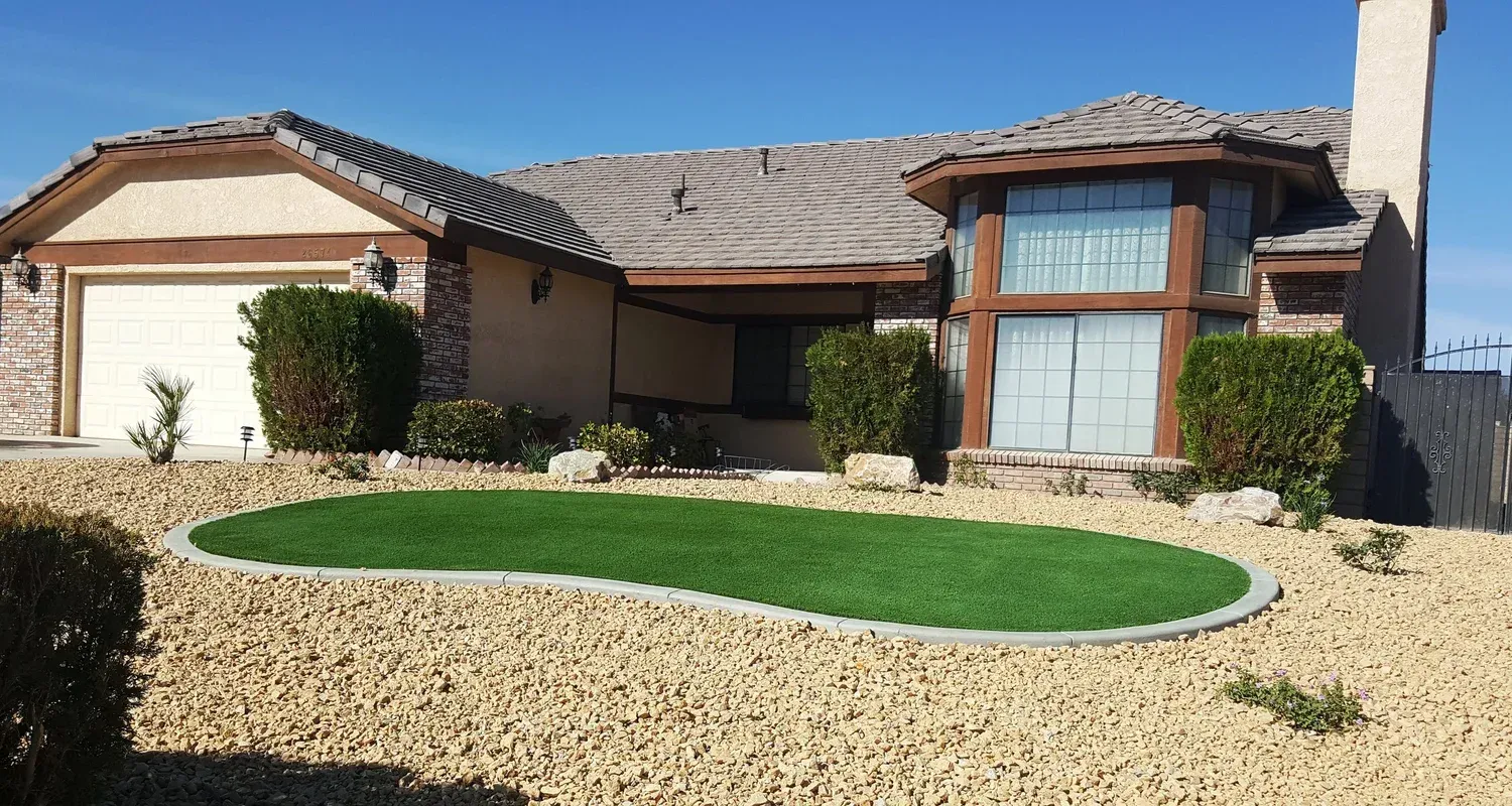 House with tan exterior, green turf lawn, and gravel landscaping under a clear blue sky.