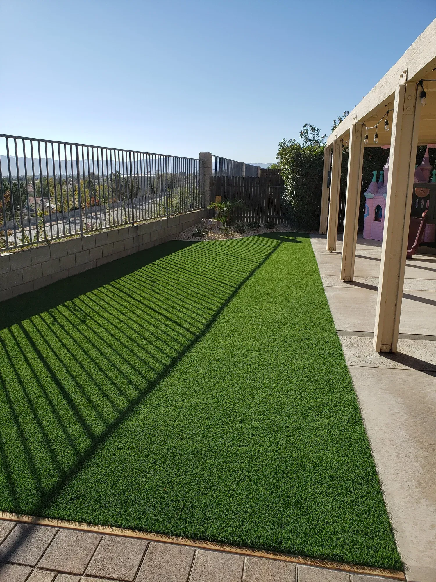 Green artificial turf yard with fence and pergola, sunny day.
