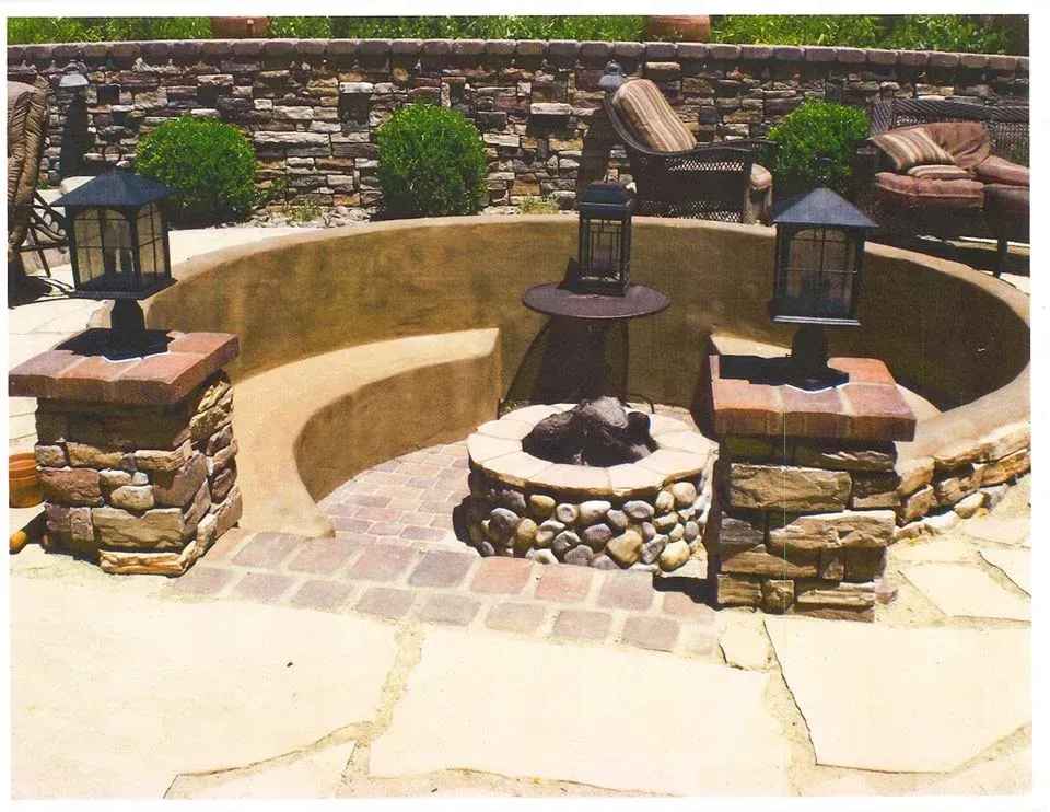 Stone patio with built-in seating around a fire pit, surrounded by a stone wall, lanterns, and outdoor furniture.