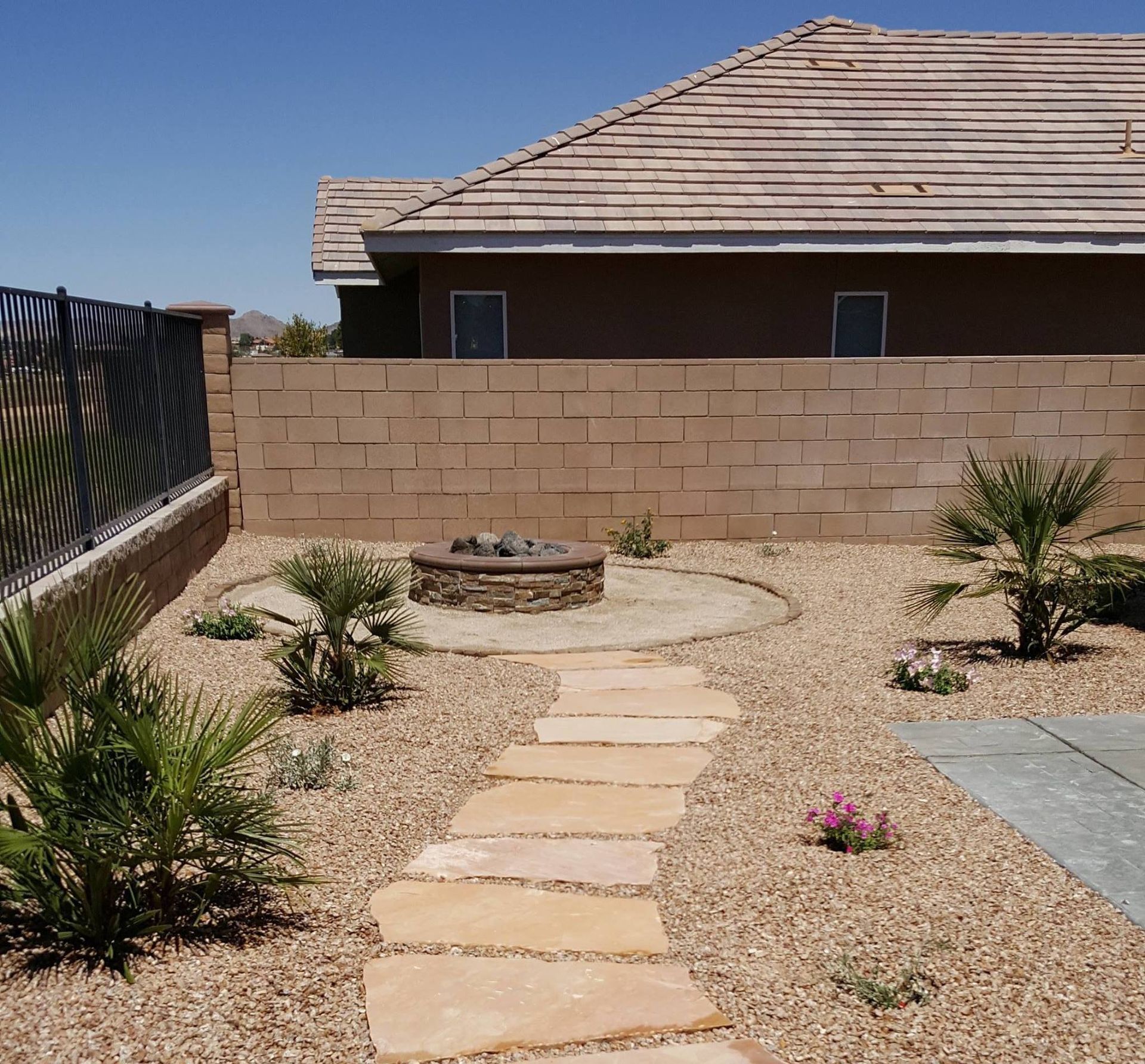 A backyard with a stone fire pit, pathway, and landscaping against a brick wall and house.