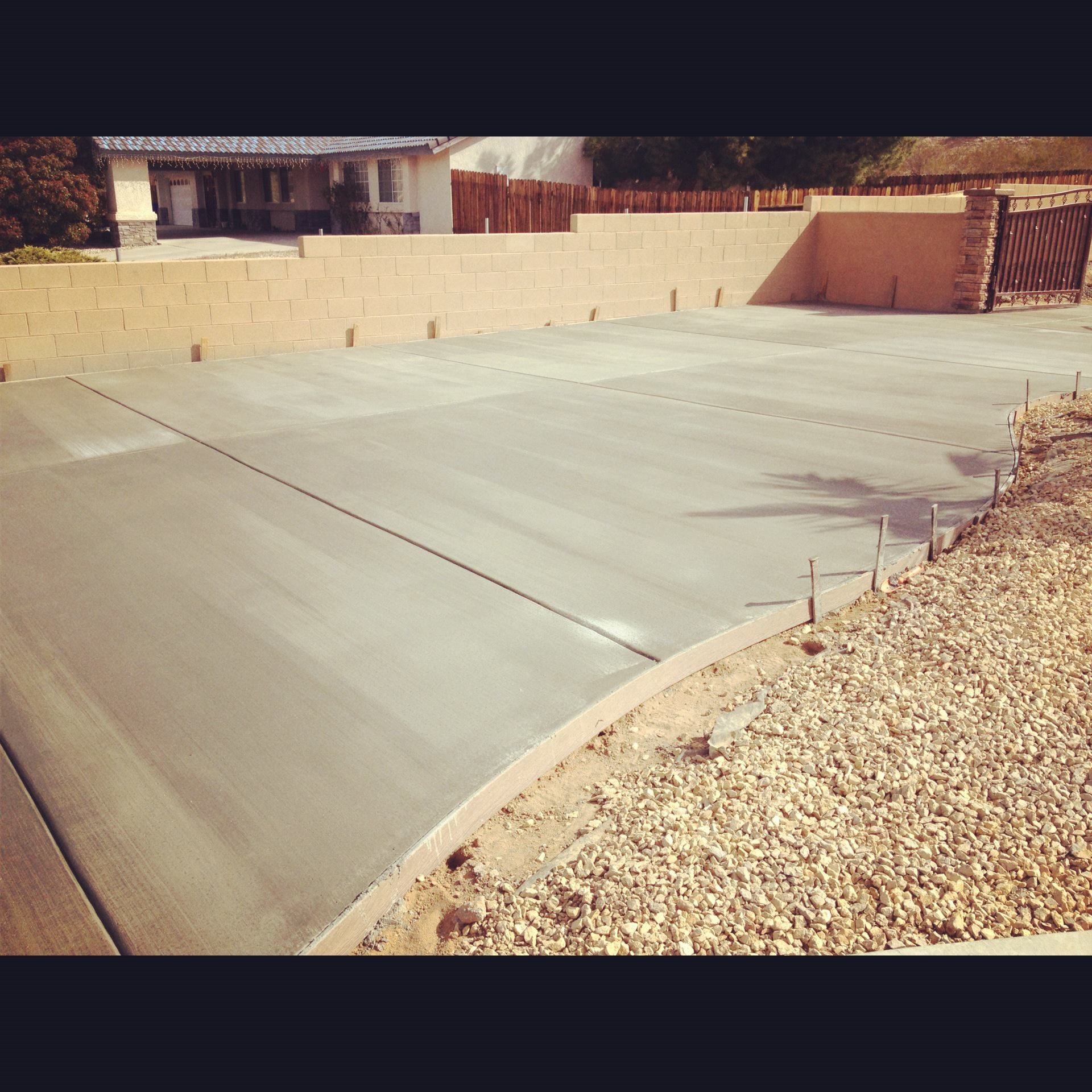 Freshly poured concrete driveway with surrounding retaining walls and gravel.