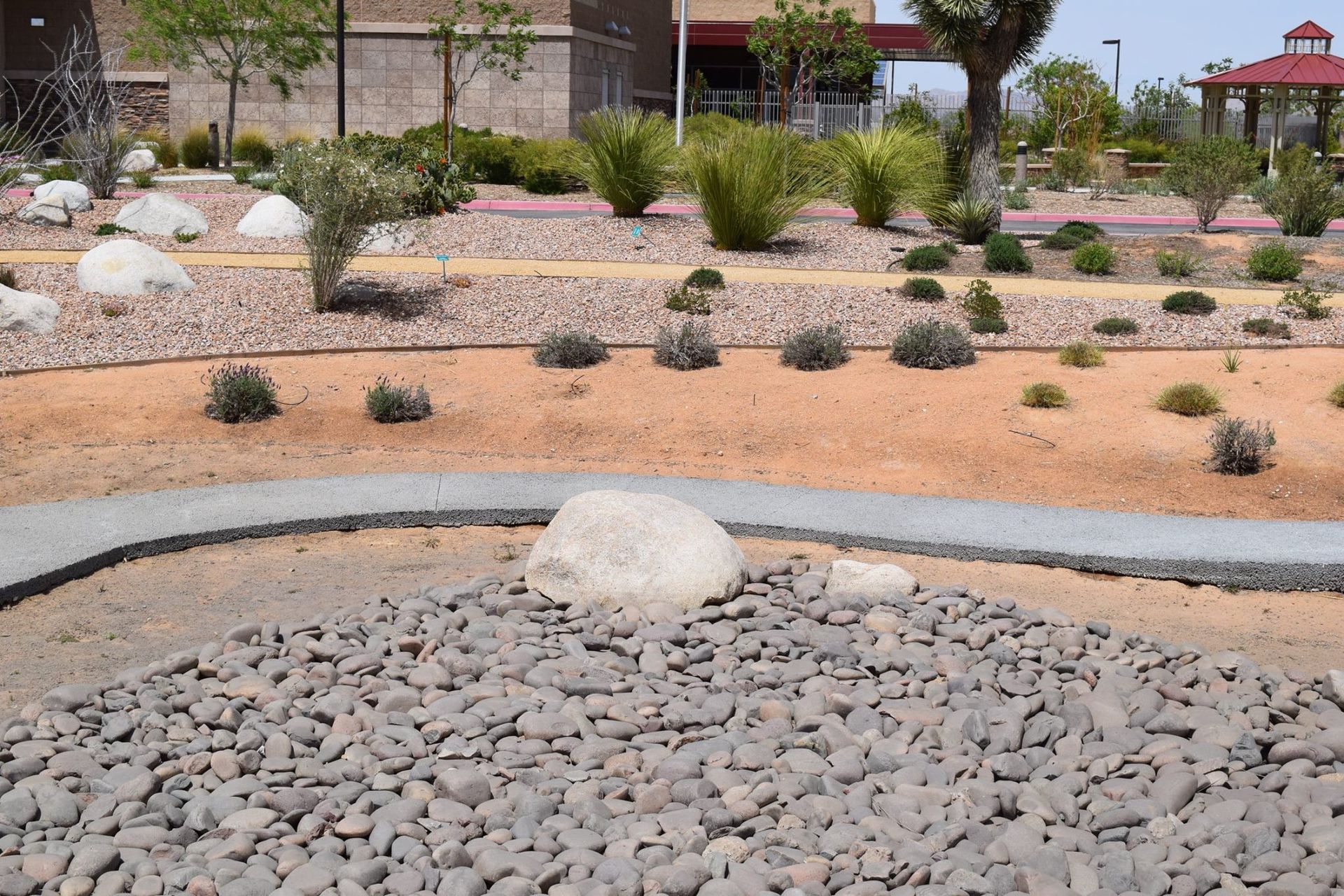 Desert landscape with gray and brown rocks, sparse green plants, and a building in the background.