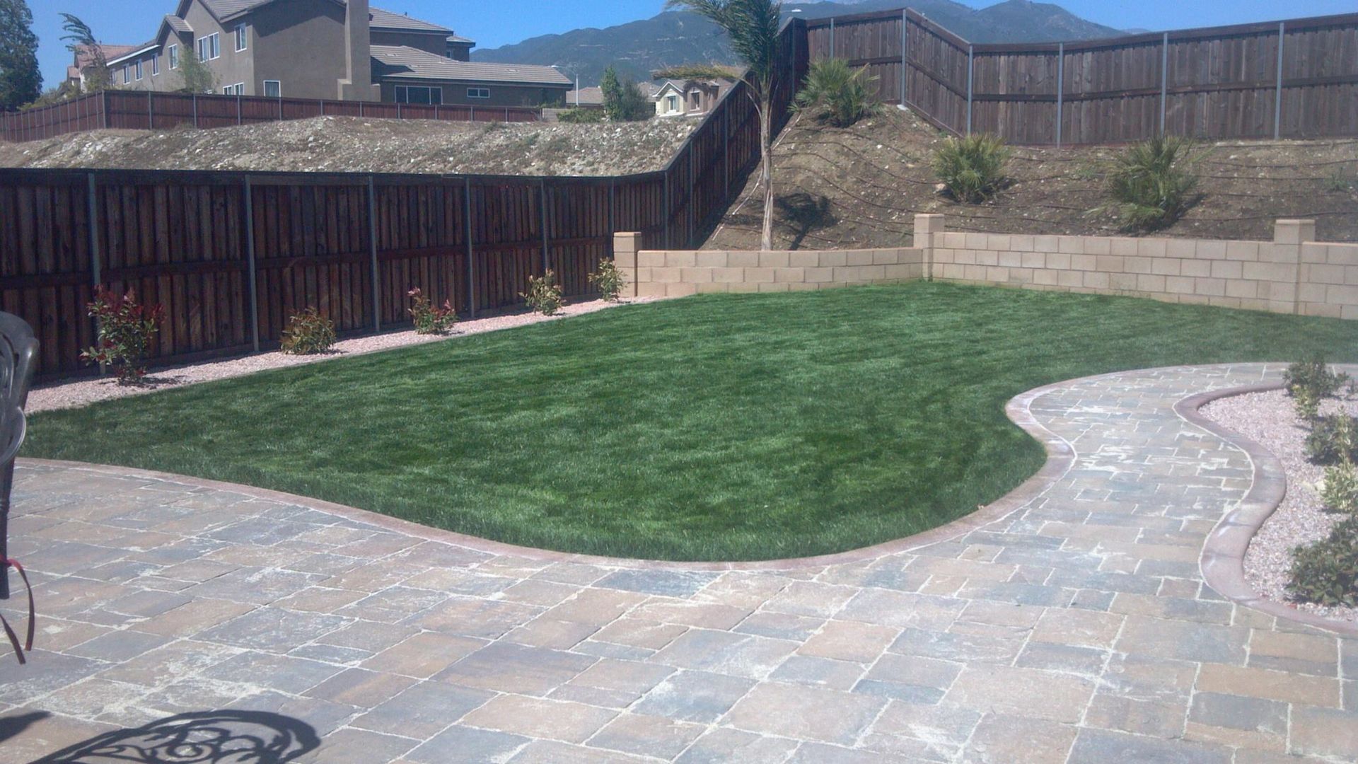 Backyard with green lawn, stone patio, wooden fence, and mountains in the background.