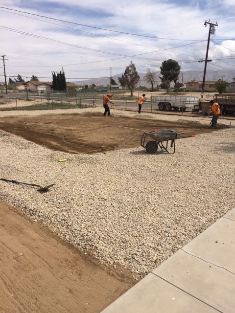 Workers leveling dirt area for a project, surrounded by gravel.