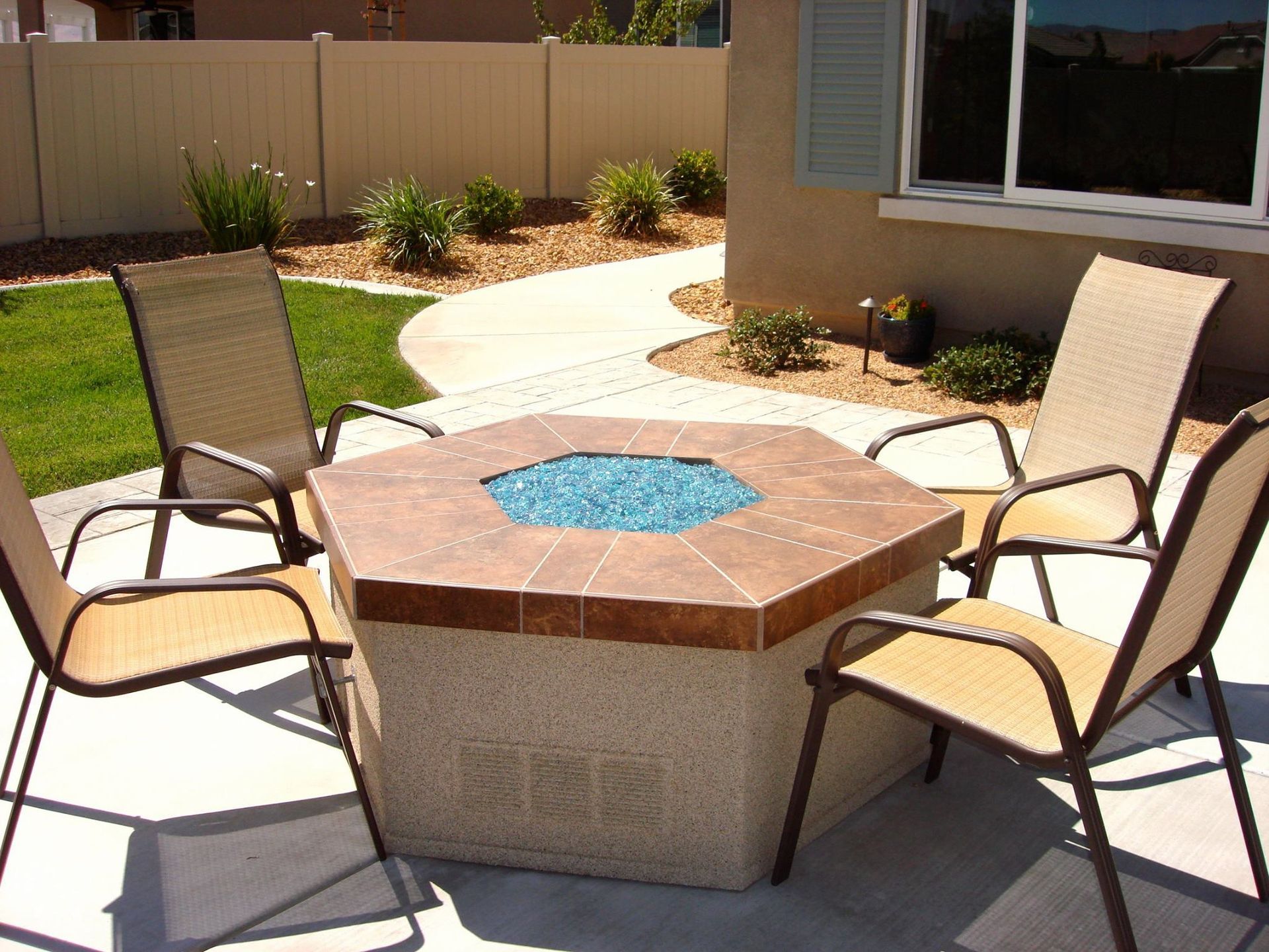 Patio with fire pit surrounded by four chairs, lawn, and fence.