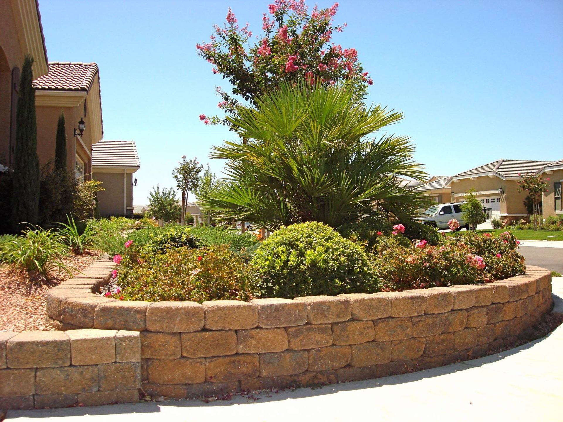 Curved brick retaining wall with lush landscaping in front of a house, under a sunny sky.