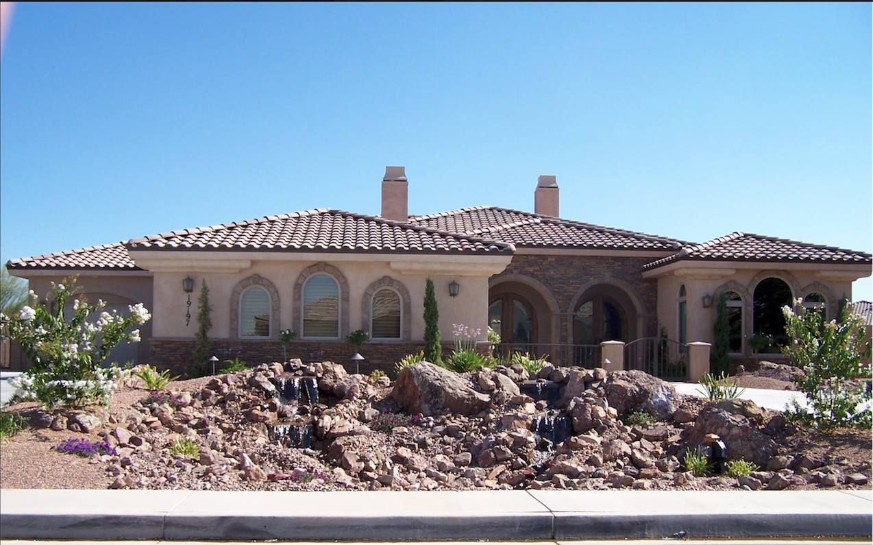 A large, beige stucco house with a tiled roof against a clear blue sky.