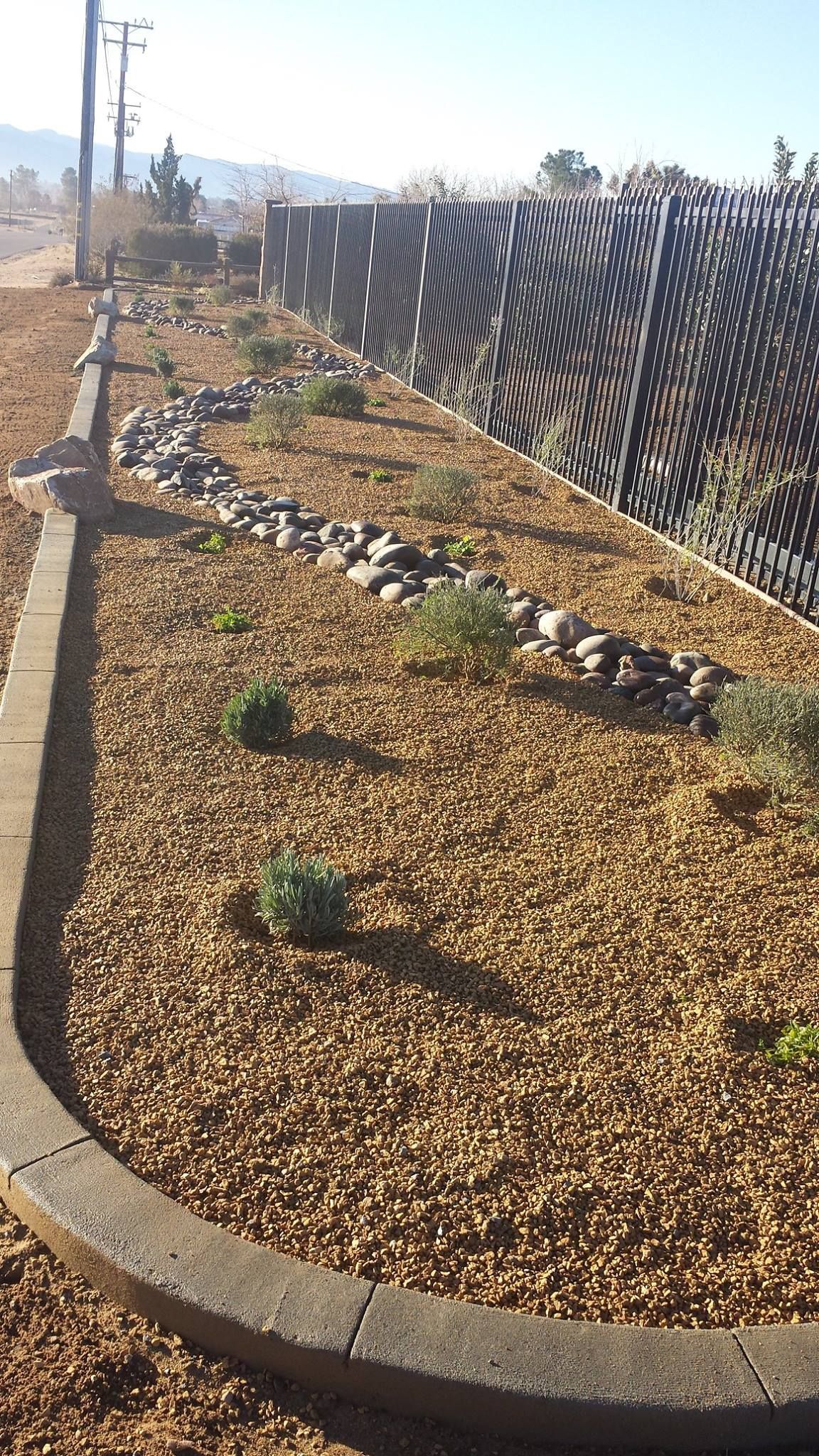 Gravel and rock garden bed alongside a patterned retaining wall, under a clear sky.