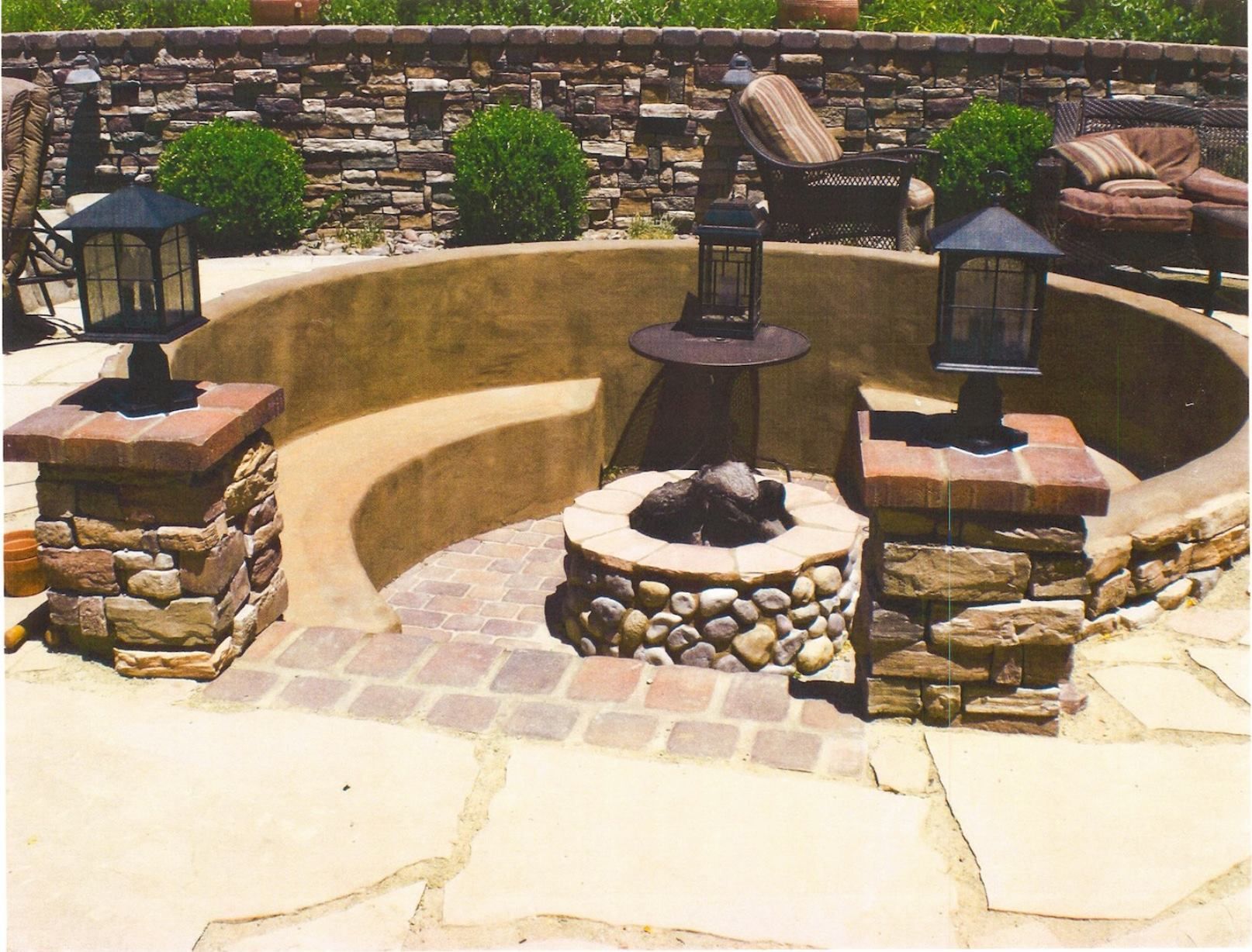 Circular outdoor fire pit area with stone benches and lamps, surrounded by a stone wall.