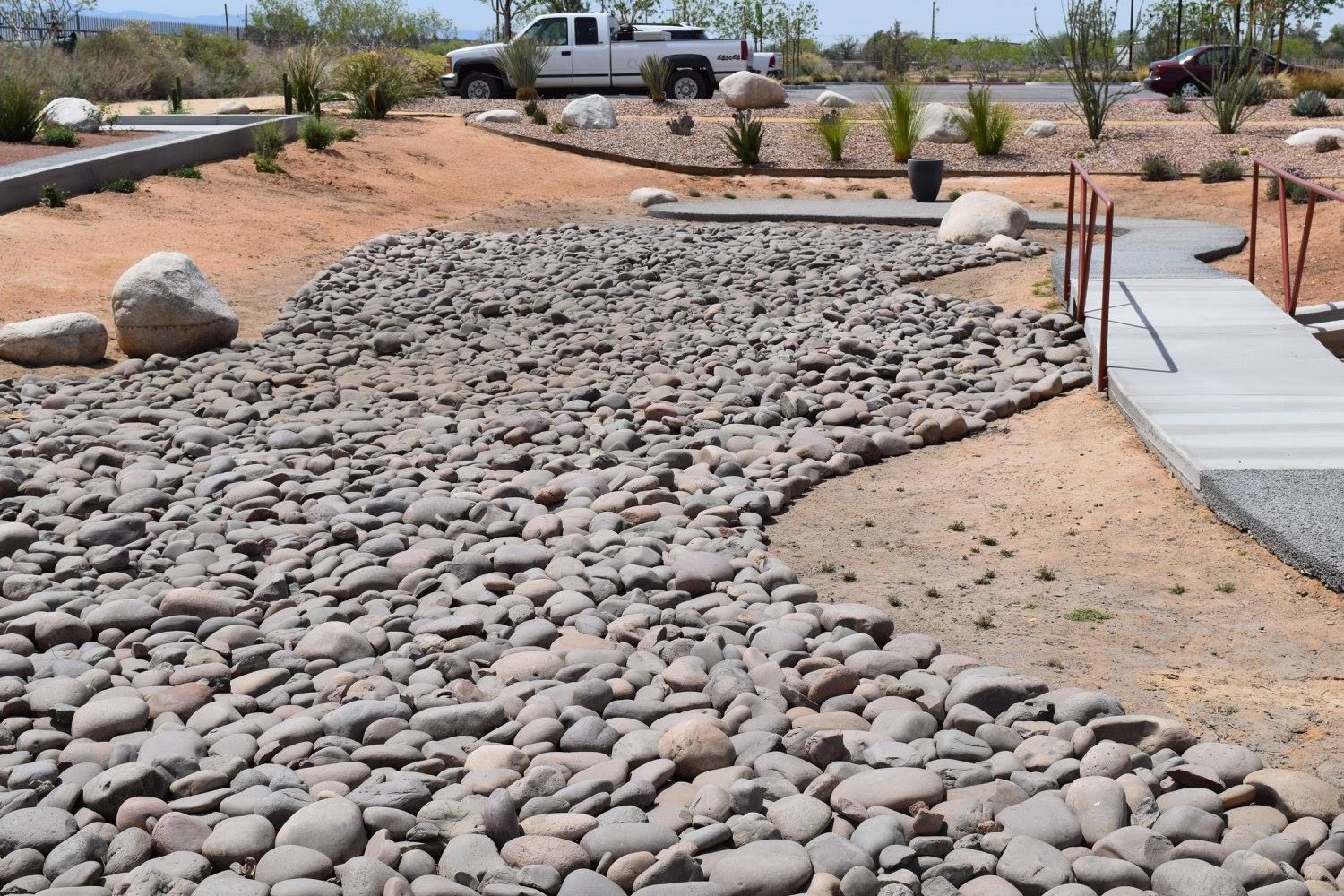 Rock-filled dry riverbed with a concrete path and small bridge in a desert landscape.