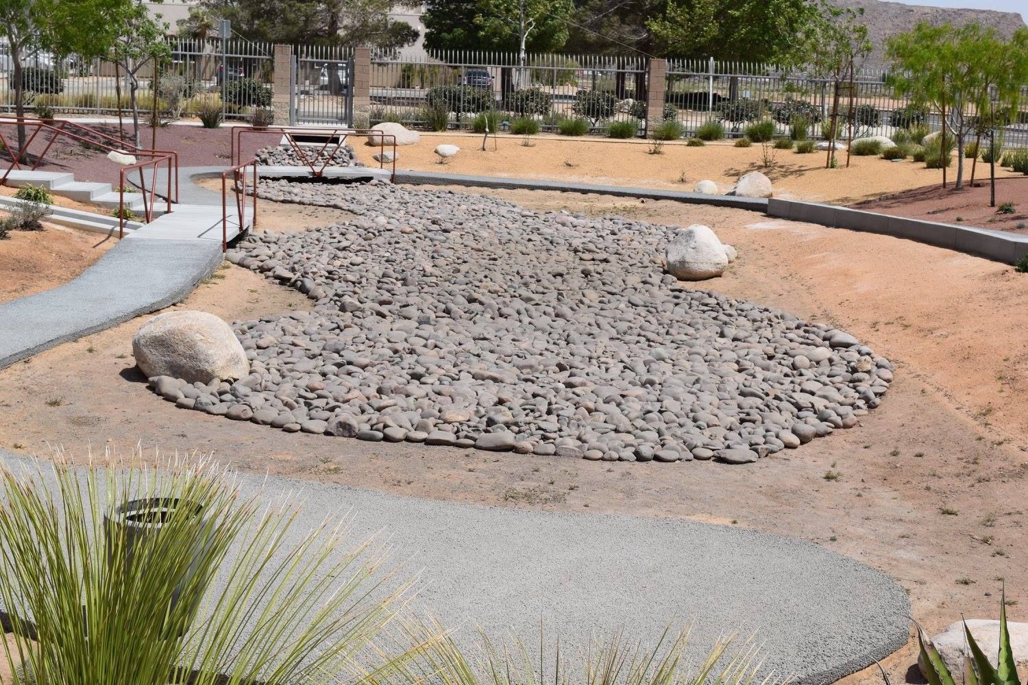 Dry riverbed with gray rocks and a walking path in a desert landscape.
