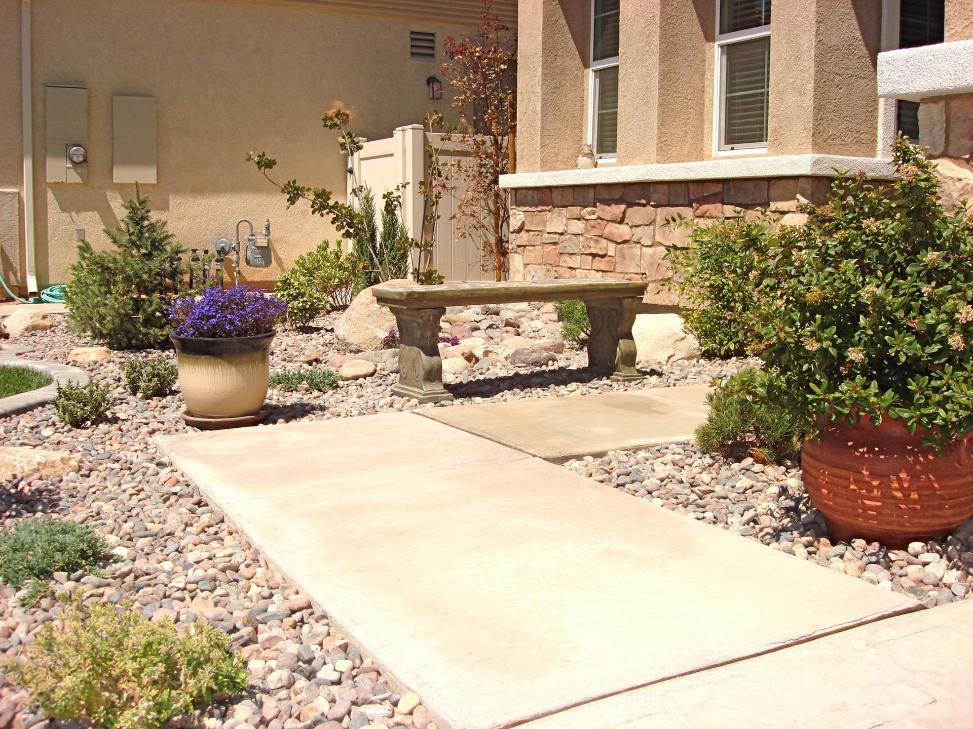 Stone walkway leading to a house with a bench and potted plants in a gravel garden.