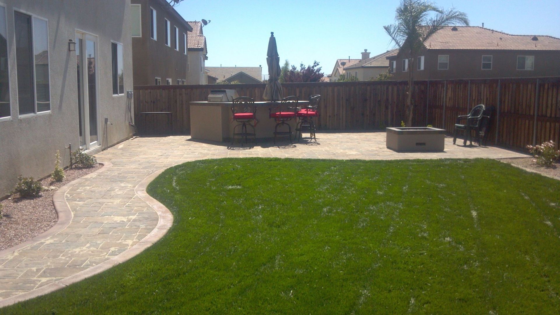 Backyard with green lawn, stone patio, bar seating, fire pit, and wooden fence.