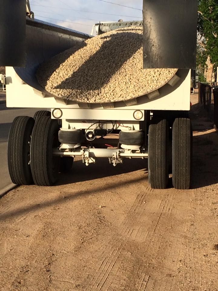 Rear view of a dump truck bed filled with gravel, tires visible on dirt road.