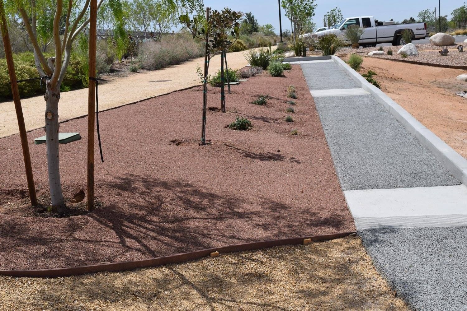 Landscaped area with trees, red gravel, gray walkway, and tan gravel.