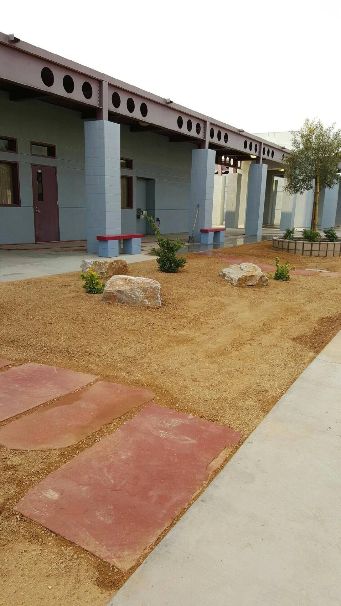 Courtyard with gravel, reddish stone pavers, and benches next to a blue building with dark beams.