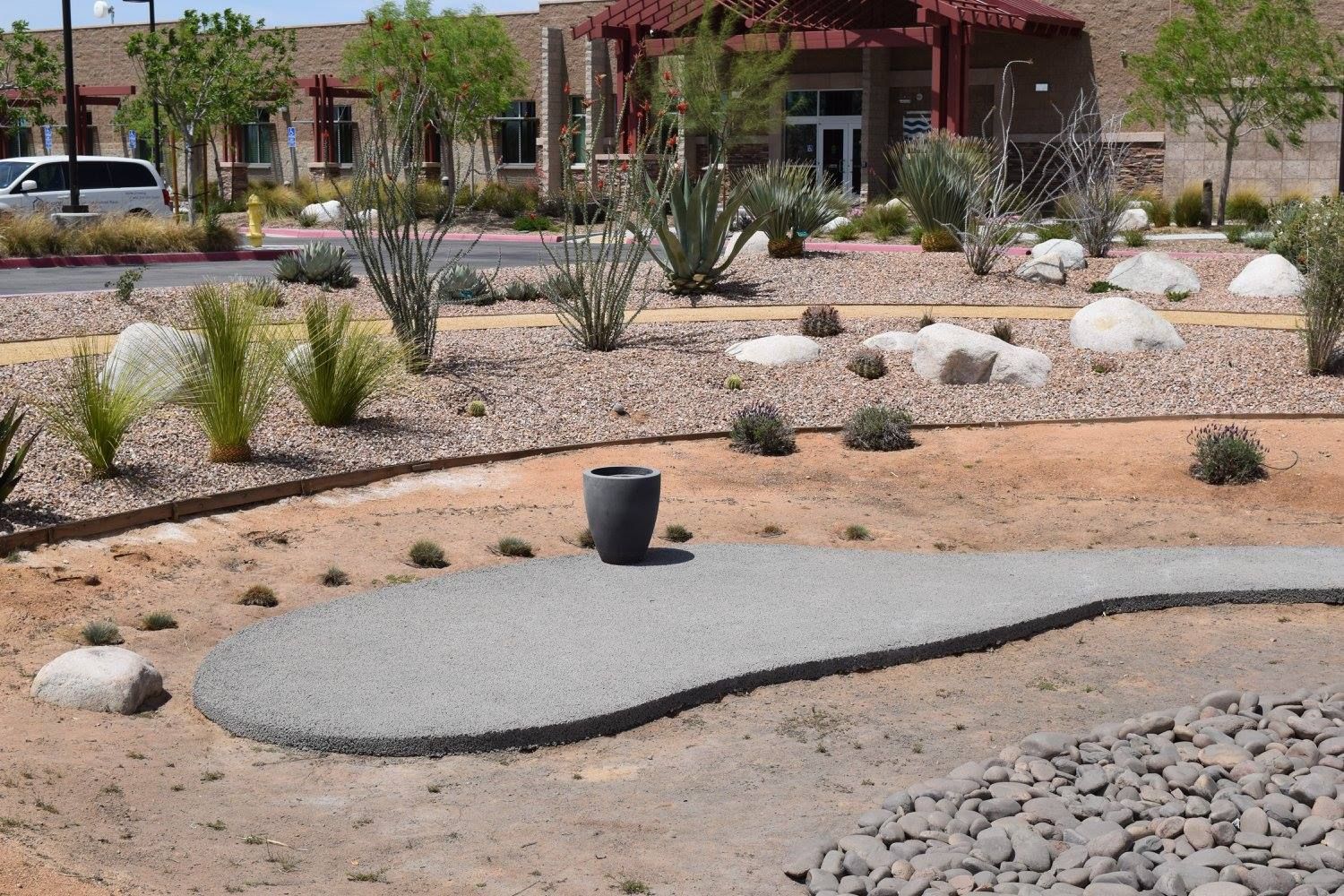 Gravel pathway with a dark gray urn in a xeriscaped landscape, with a building in the background.