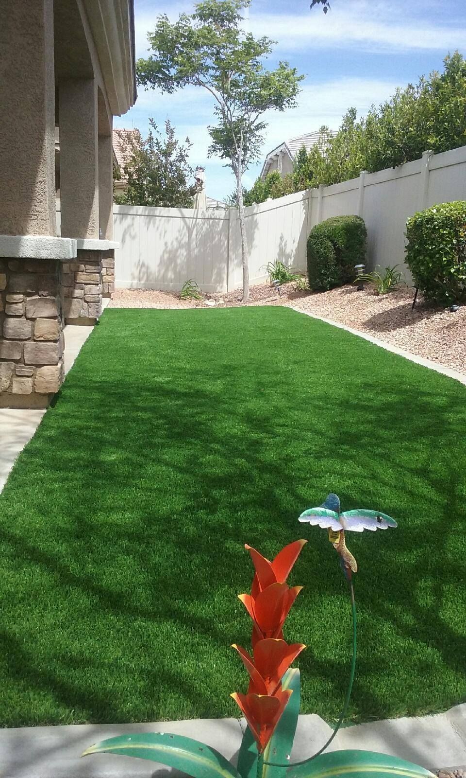 Green artificial turf backyard with decorative metal flower and white fence.