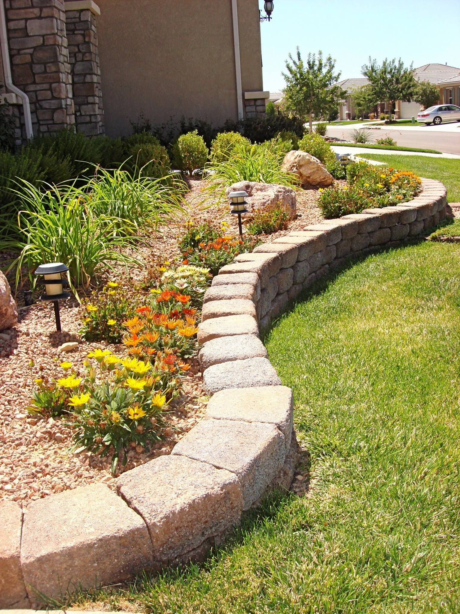 Curved stone retaining wall with colorful flowers and shrubs in a landscaped front yard.