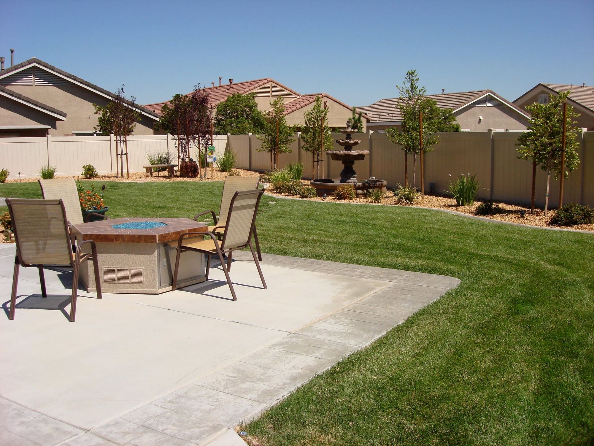Backyard with patio, fire pit, lawn, landscaping, and a fountain on a sunny day.