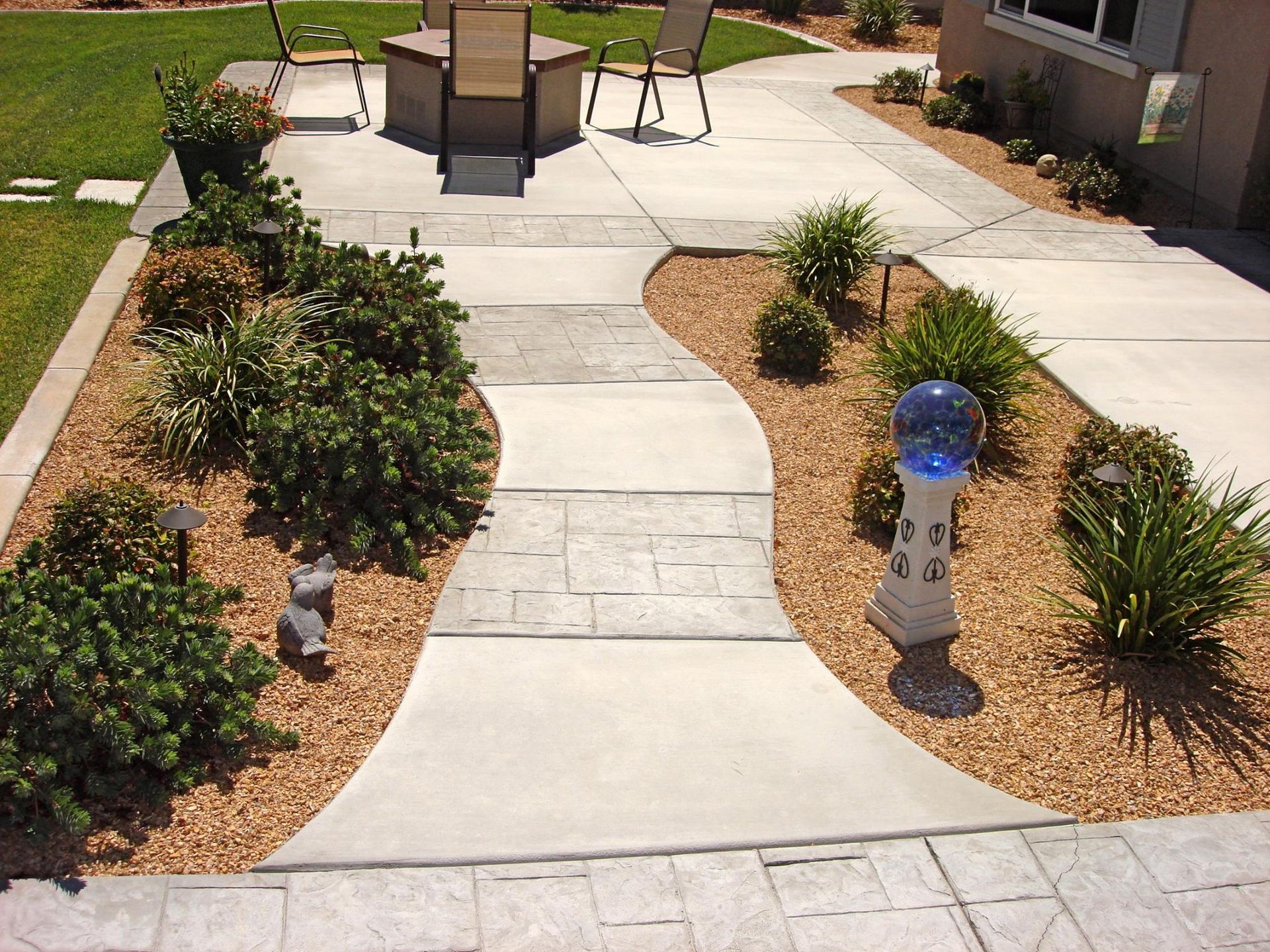 Concrete patio with winding walkway, surrounded by landscaping, plants, and decorative lights.