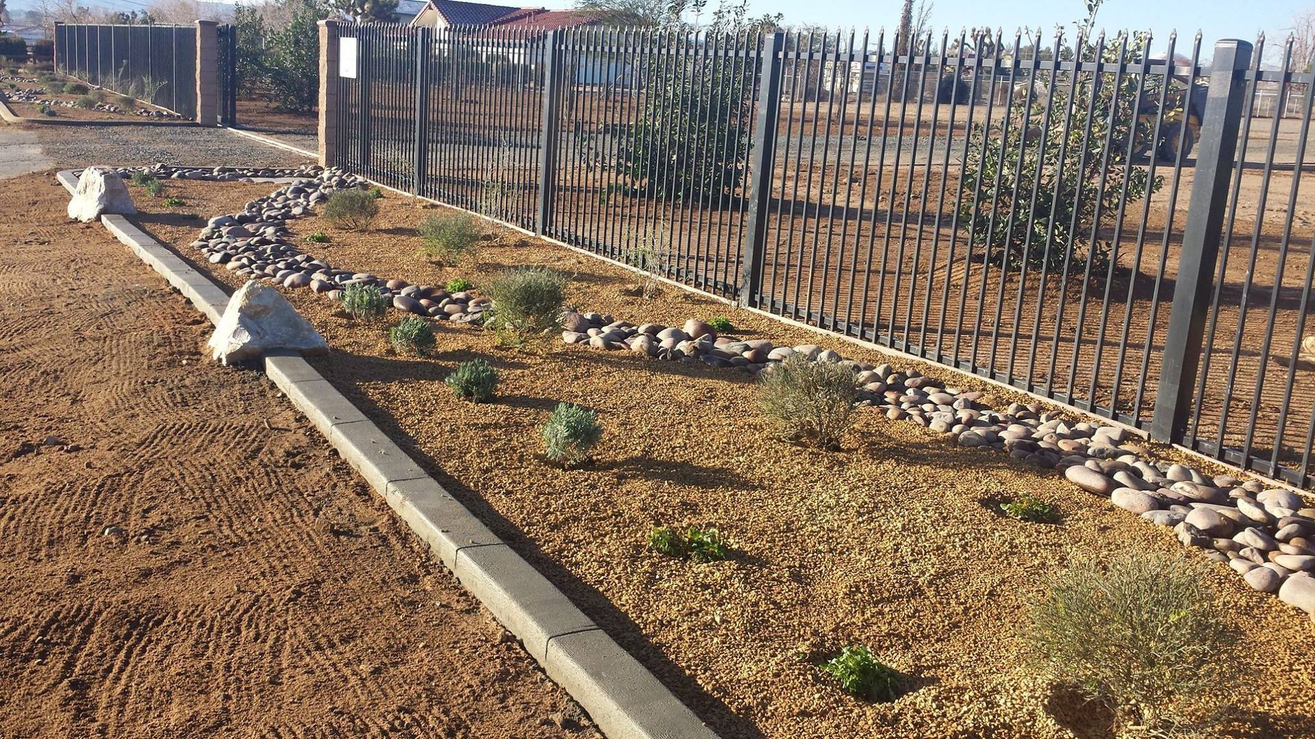 Landscaped yard with gravel, plants, rocks, and black metal fence.