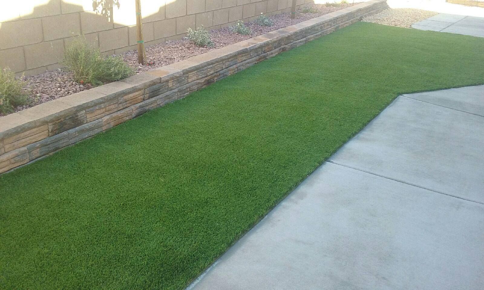 Green artificial turf next to a concrete walkway and a low retaining wall with plants.