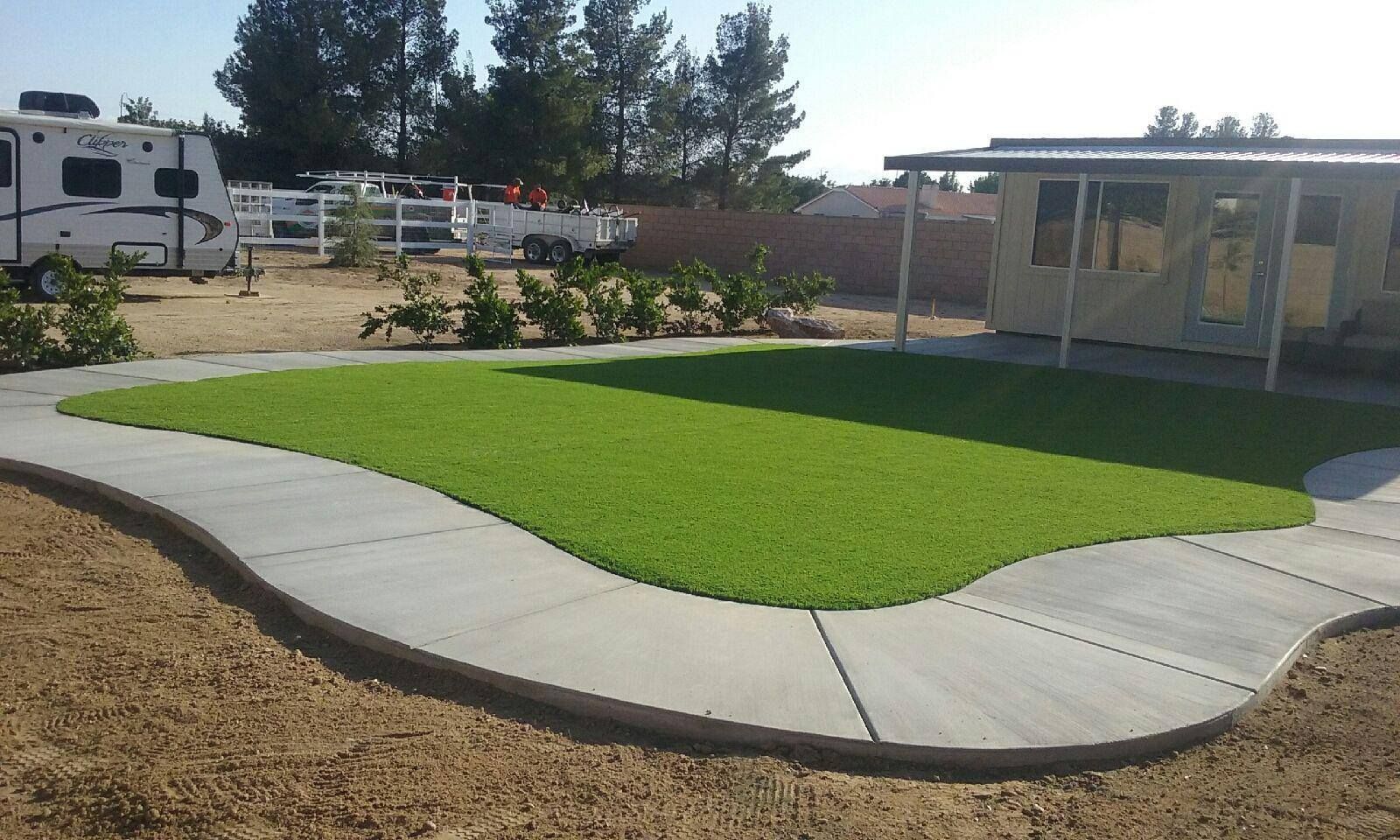 Concrete path curves around a patch of green grass in a yard. A small building and RV are in the background.
