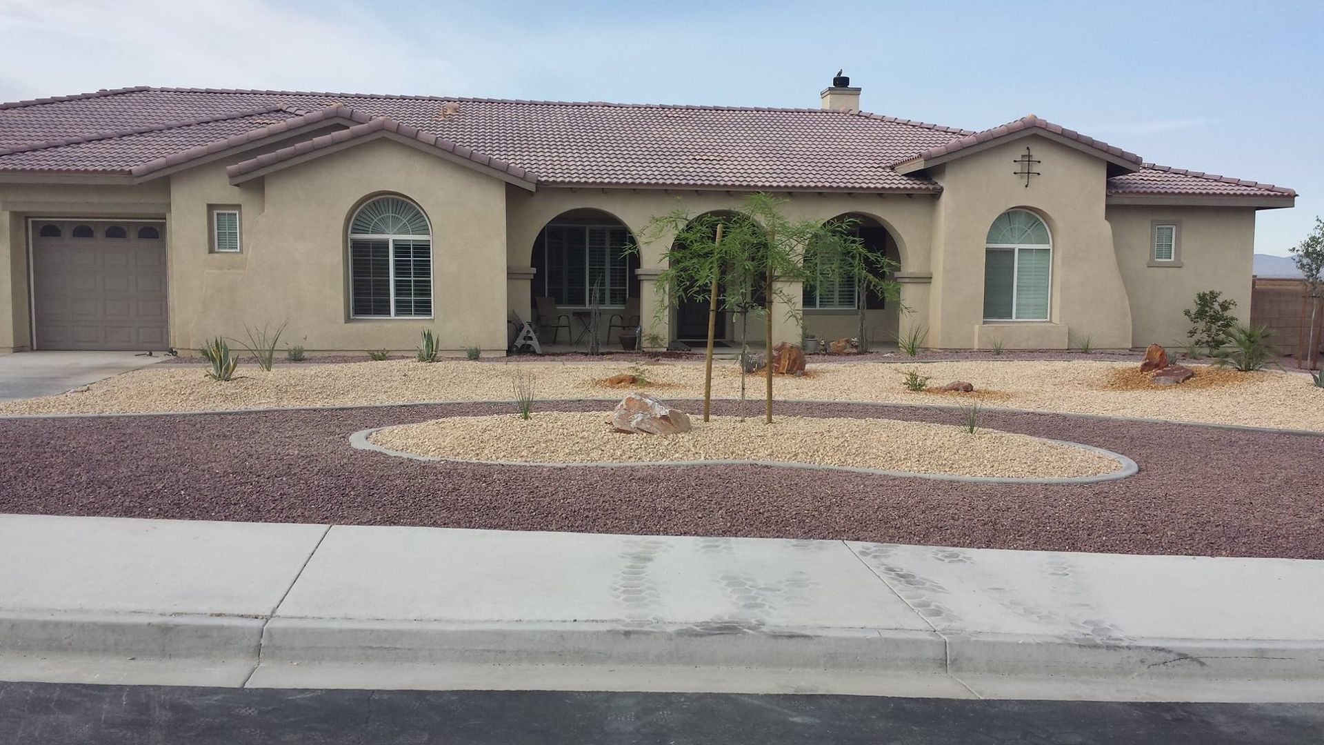 Beige stucco home with tile roof, gravel landscaping, and three young trees.
