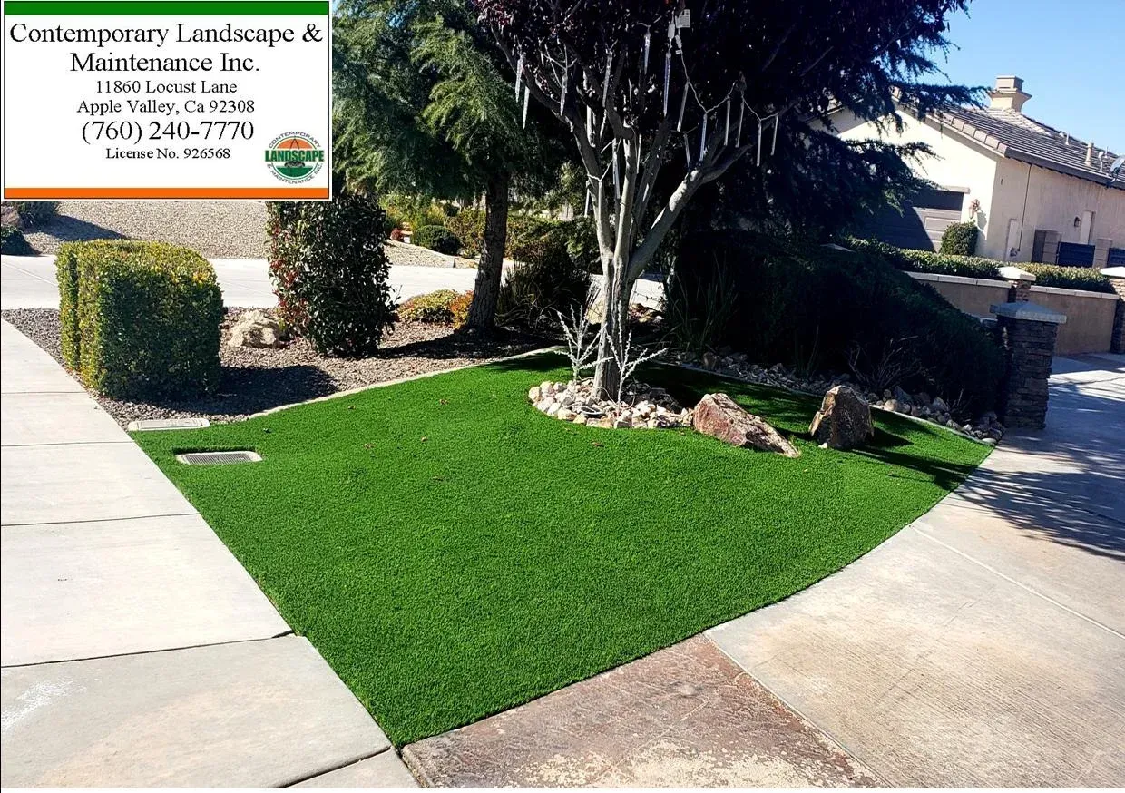 Lush green turf landscaping with tree, rock accents, and a business logo in a residential setting.