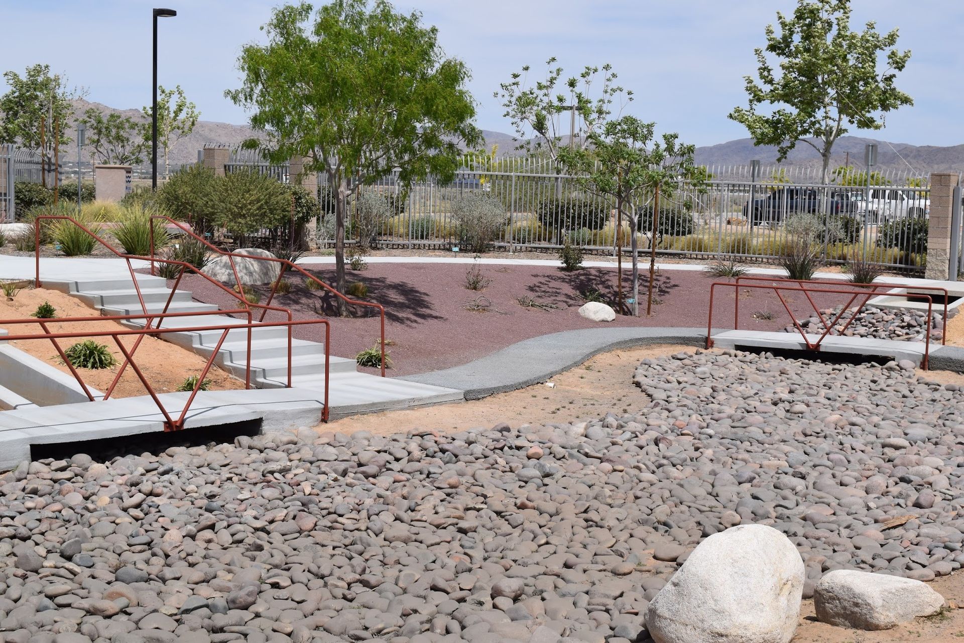 Park with gravel paths, bridges, and tiered seating, surrounded by drought-tolerant landscaping and trees.
