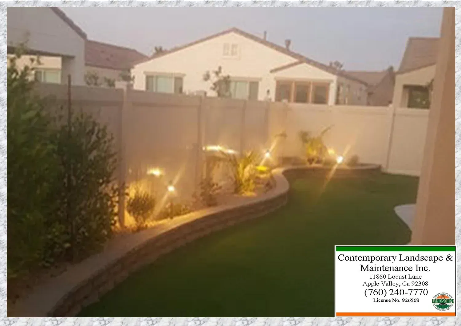 Backyard with illuminated landscaping, artificial turf, and a retaining wall.