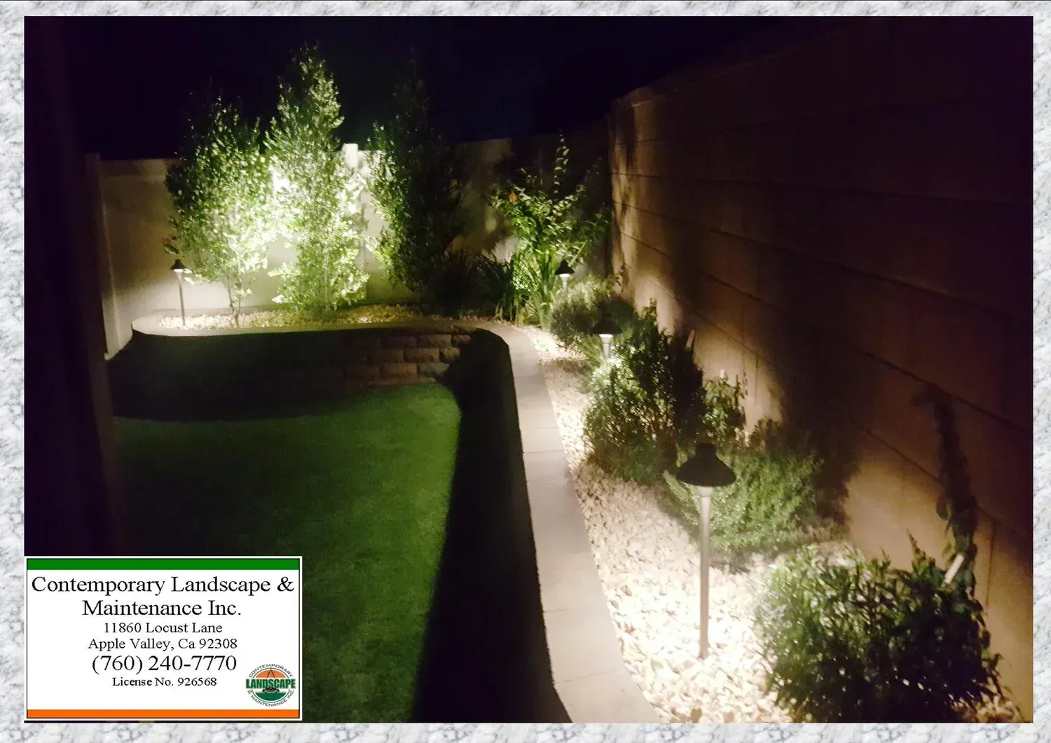 Nighttime landscape with illuminated trees, pathway, and shrubs.