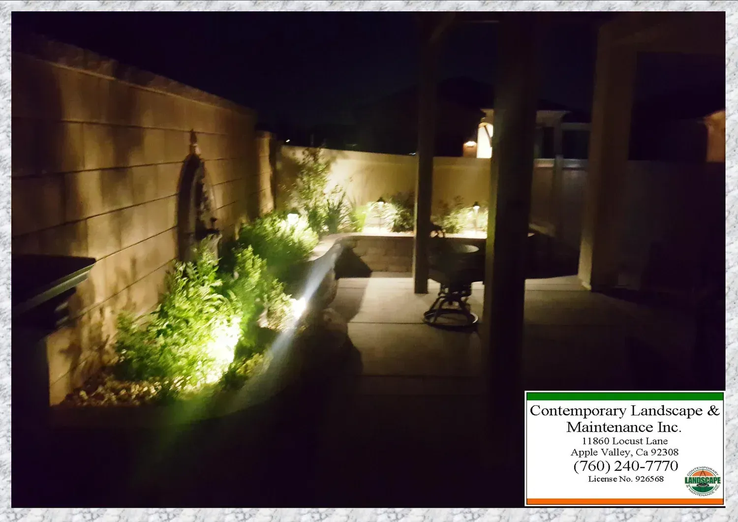 Outdoor patio with up-lit plants and wall, under an awning at night.