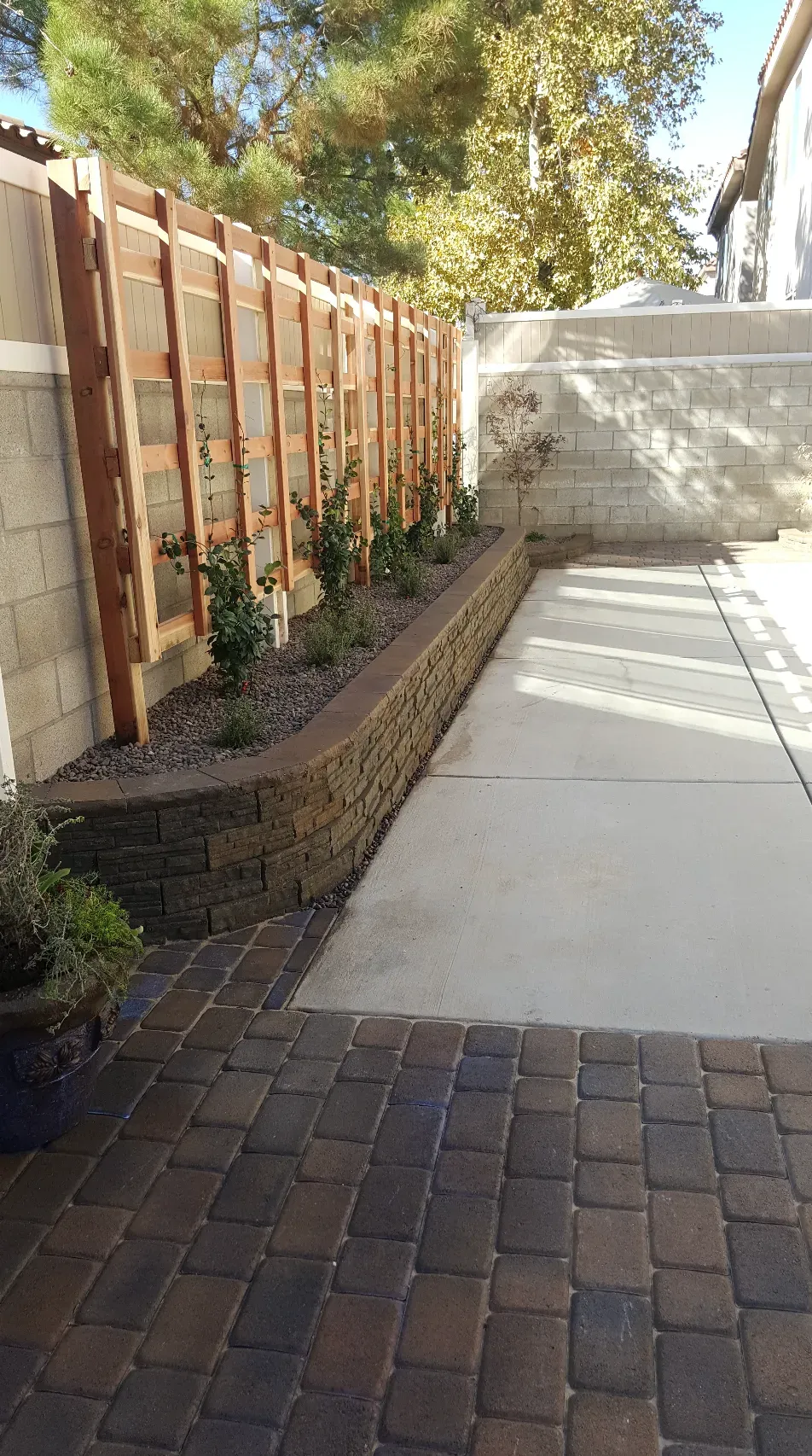 A backyard with a retaining wall, garden, concrete path, and wooden fence.